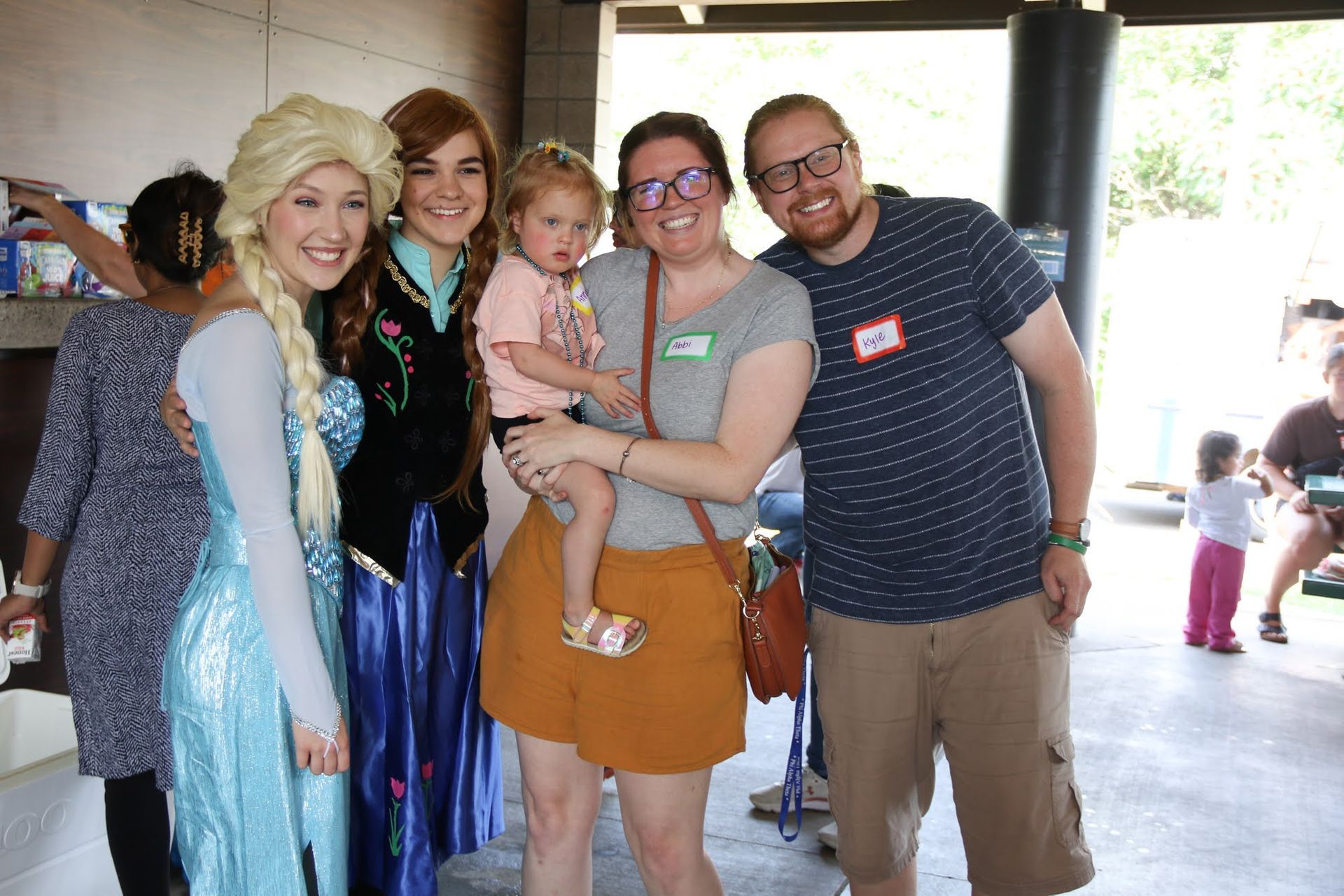 Elsa and Anna with a family at an outdoor event, people smiling for photo.