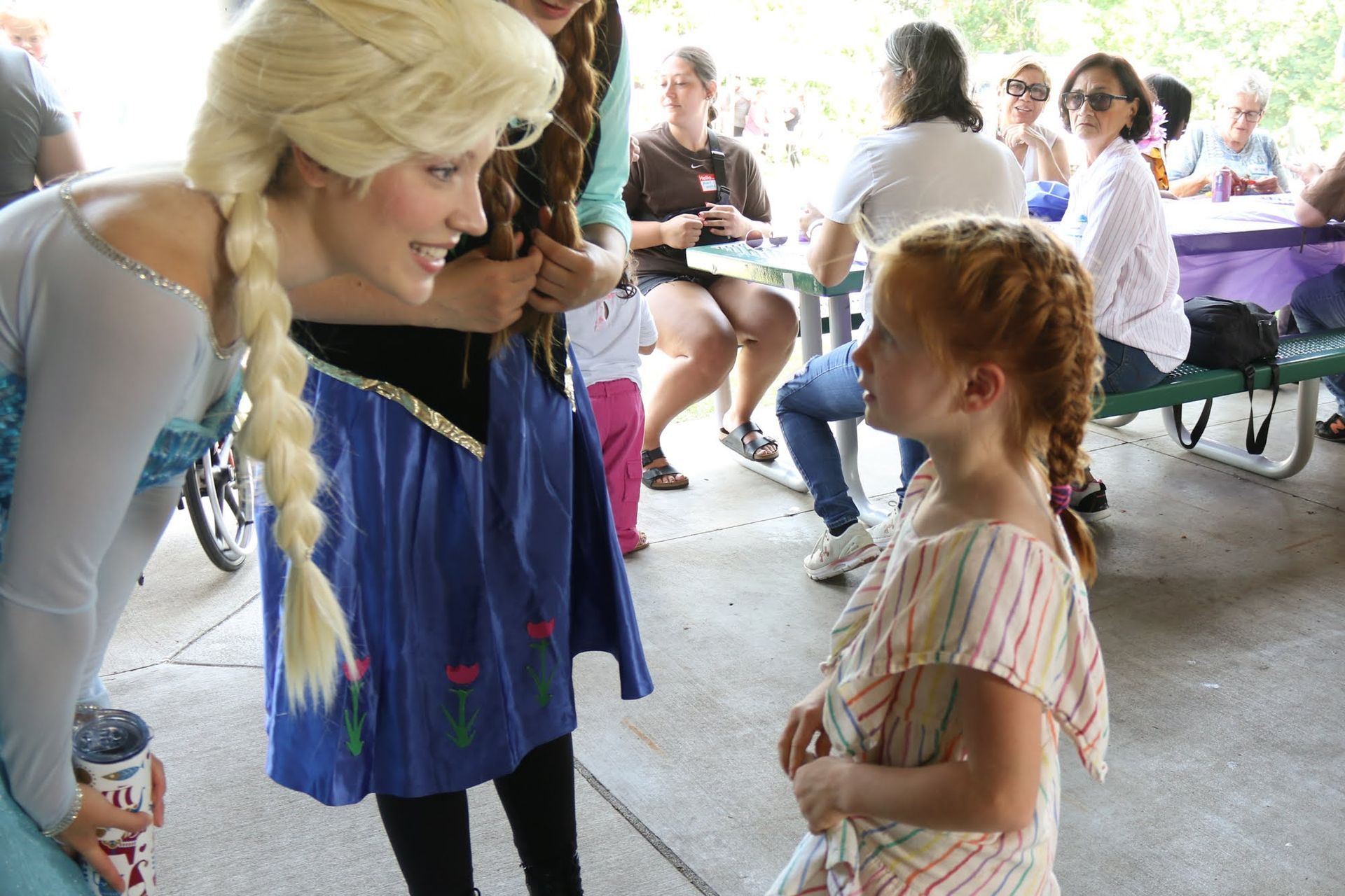 Elsa from Frozen talks to a young girl. They're both outdoors.