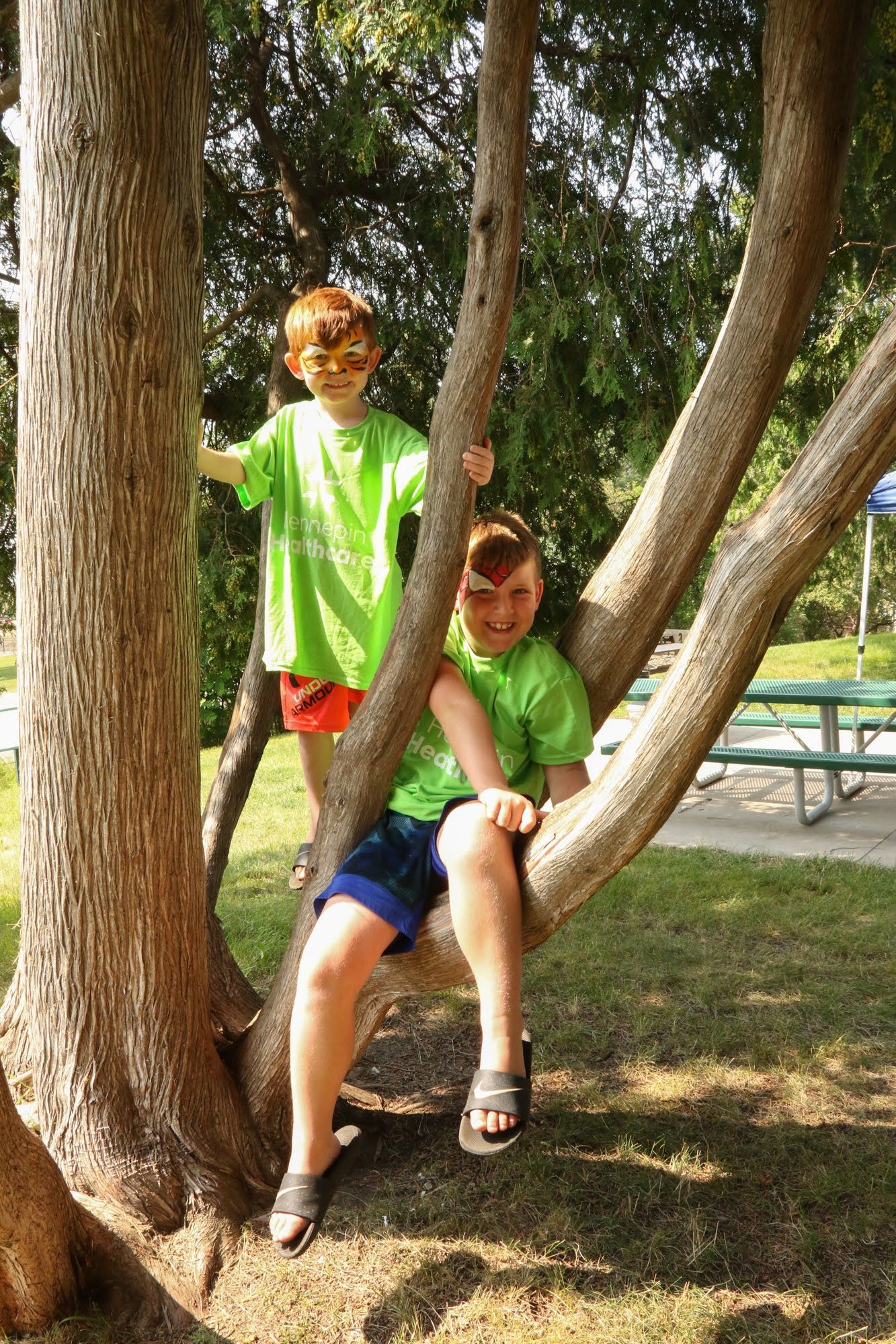Two children in green shirts climb a tree in a park.