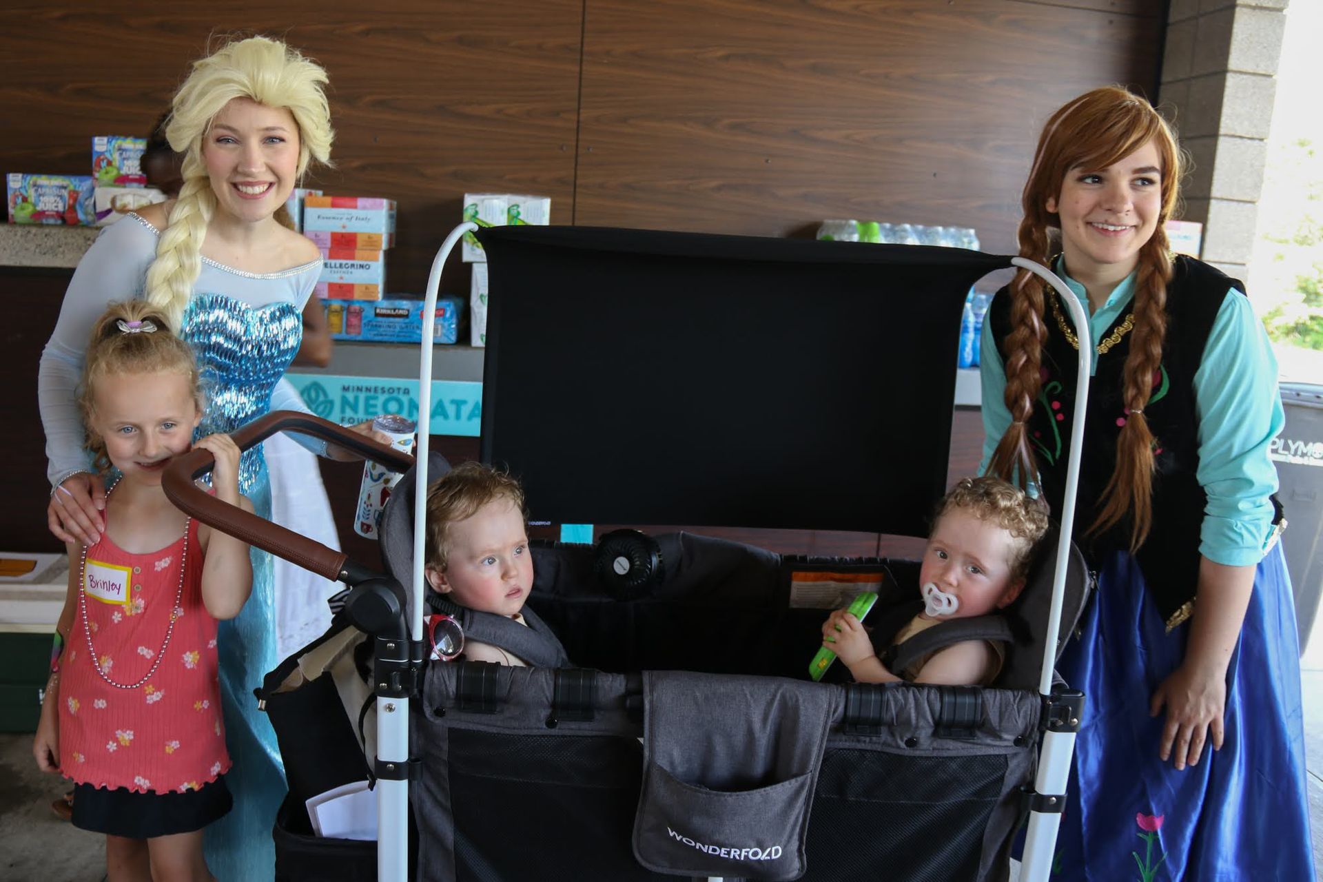 Elsa and Anna with children in a stroller. Outdoor setting. The children are dressed in casual clothes.