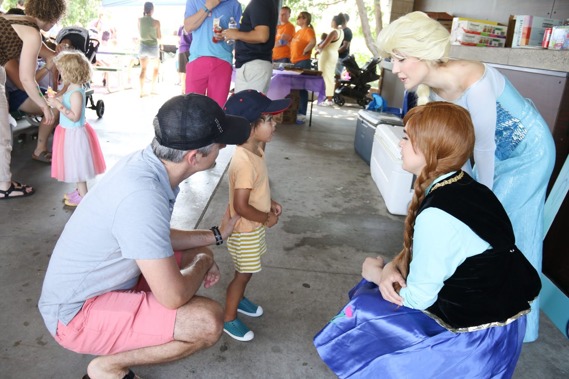 A man and child talking to people dressed as Elsa and Anna from Frozen at an outdoor event.
