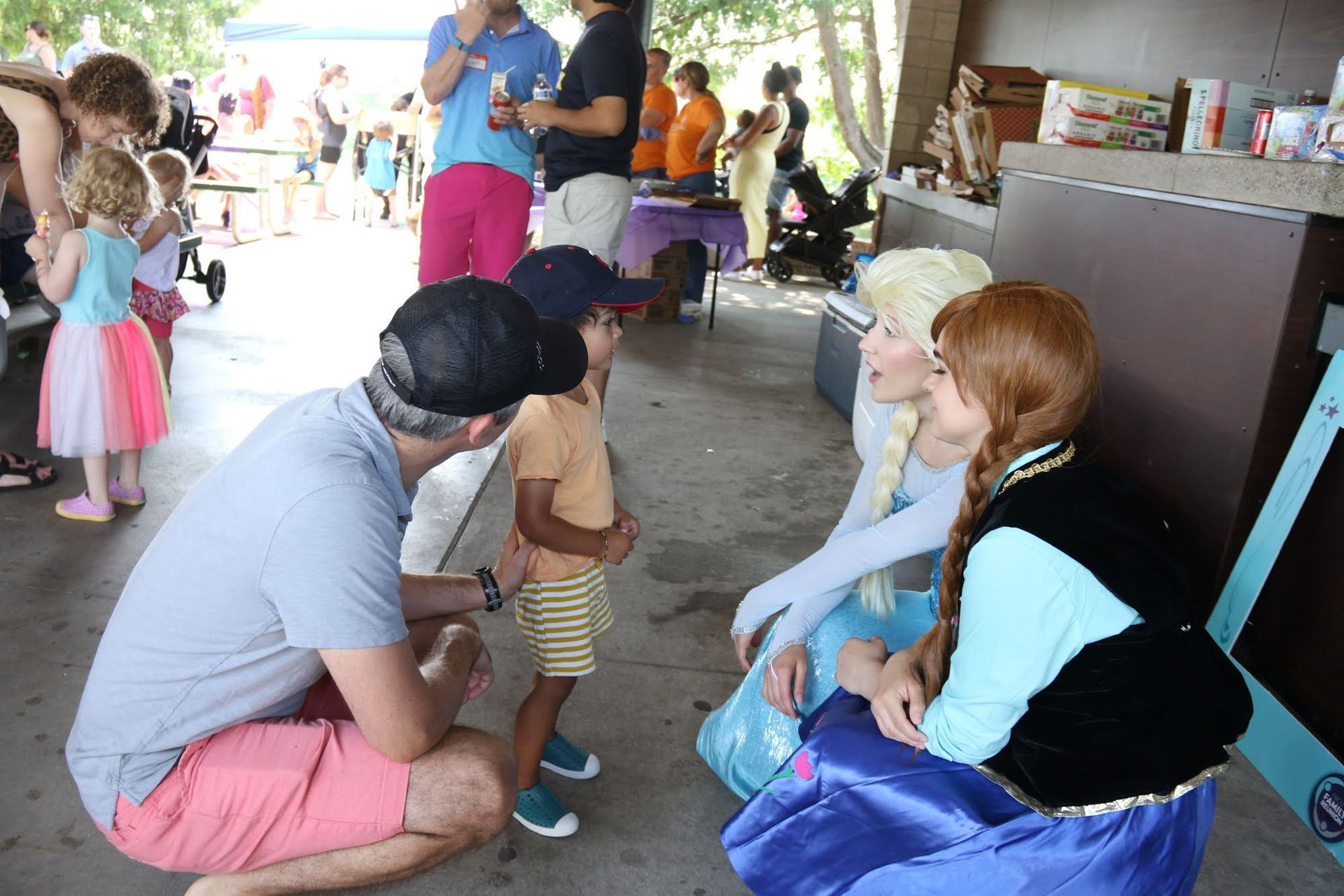 Man and child talking to Elsa and Anna characters at an outdoor event.