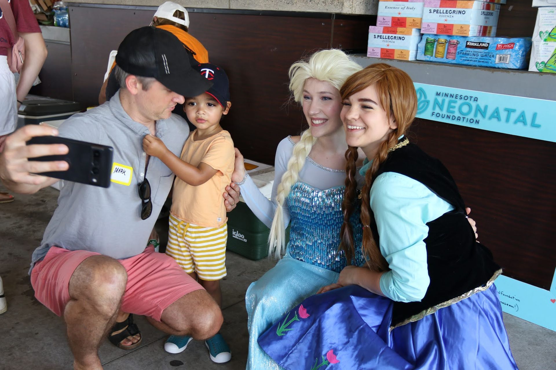 Man and child take selfie with costumed Elsa and Anna at event.