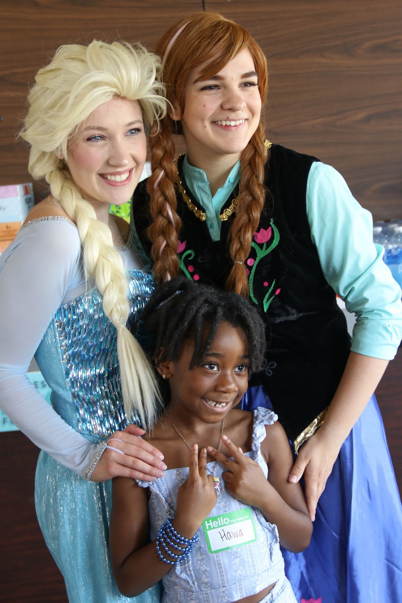 Girl poses with two women dressed as Elsa and Anna from Frozen.