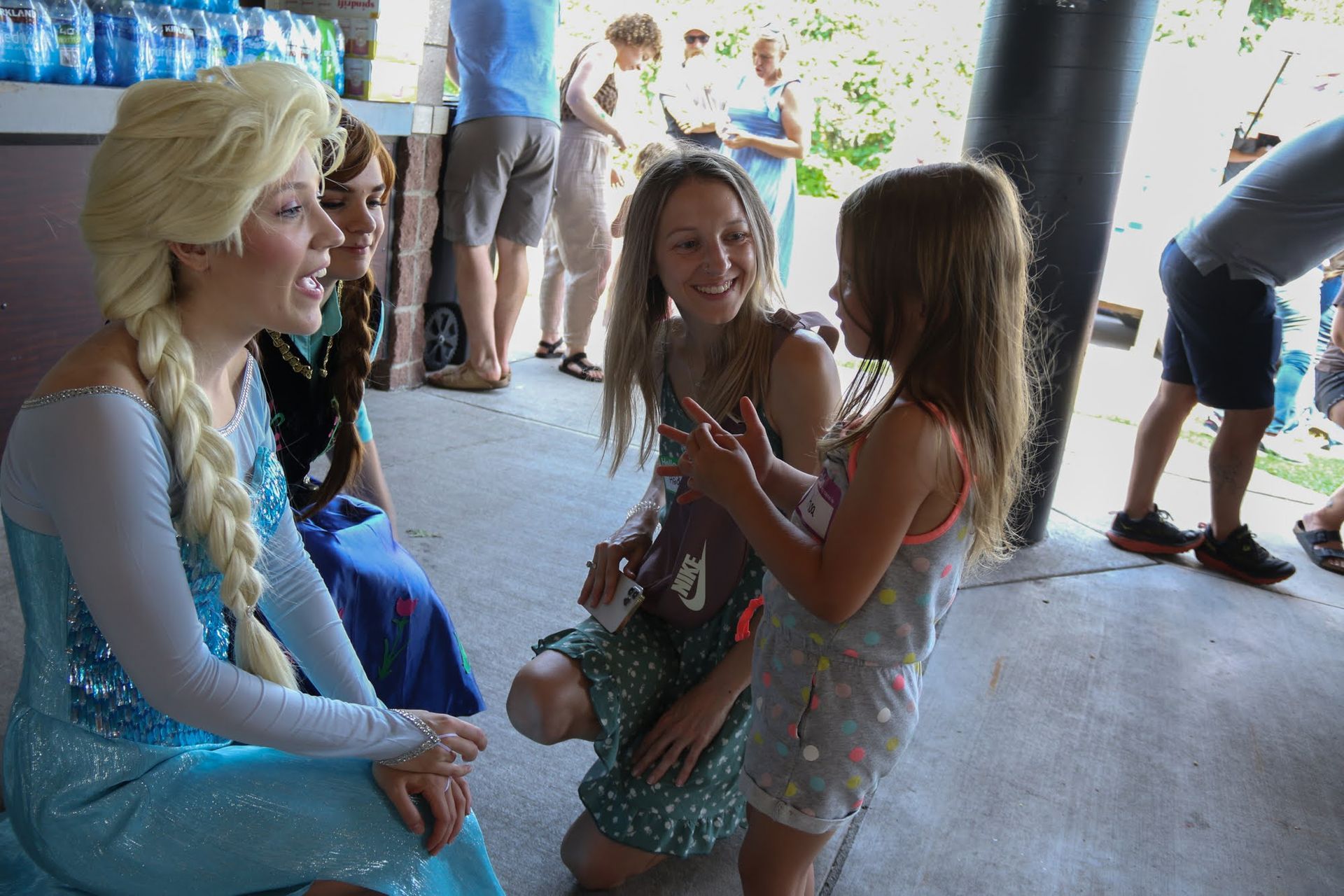 Elsa from Frozen talks to a girl, joined by woman in green polka dots, at outdoor event.