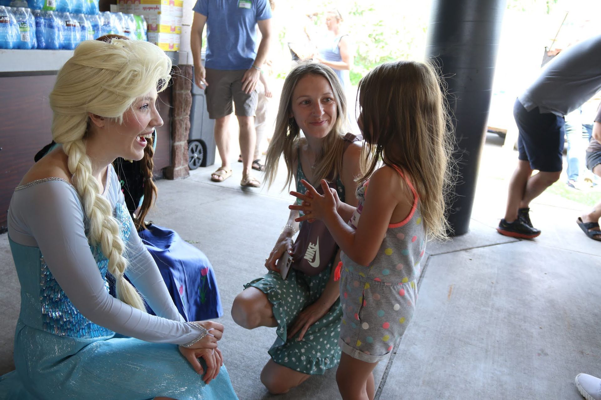 Elsa character from Frozen interacts with two young girls at an event.