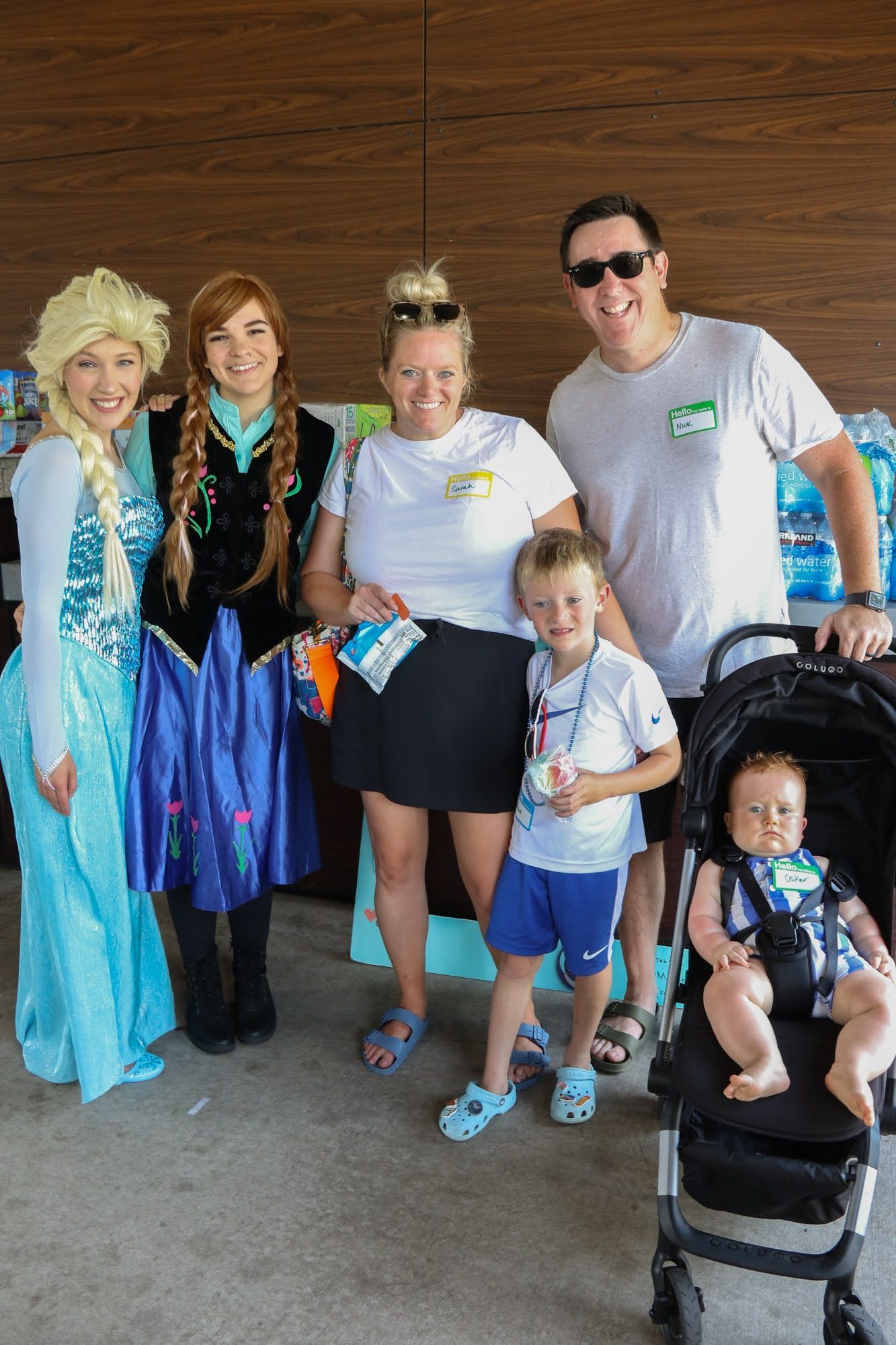 Family poses with Elsa and Anna characters at an outdoor event.