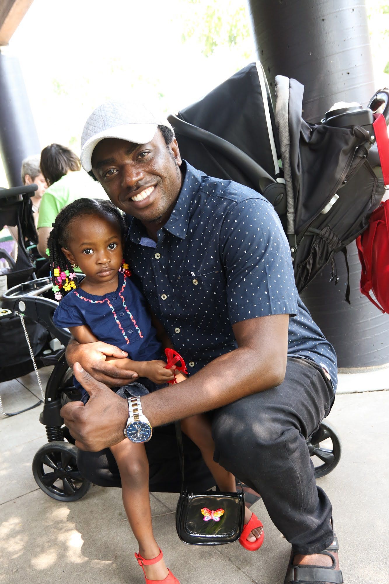 Man and child seated near a stroller. Man gives a thumbs up. Both are smiling.