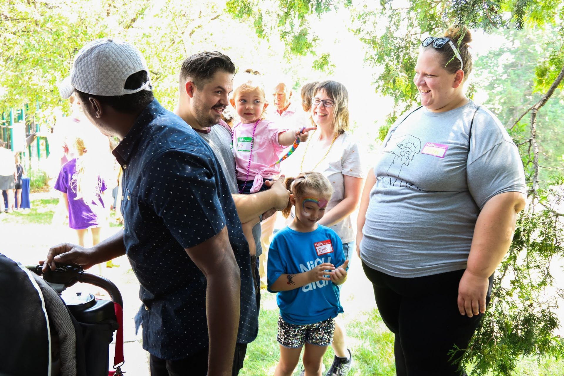 People gathered outdoors near a stroller, interacting with children. One child wears face paint.