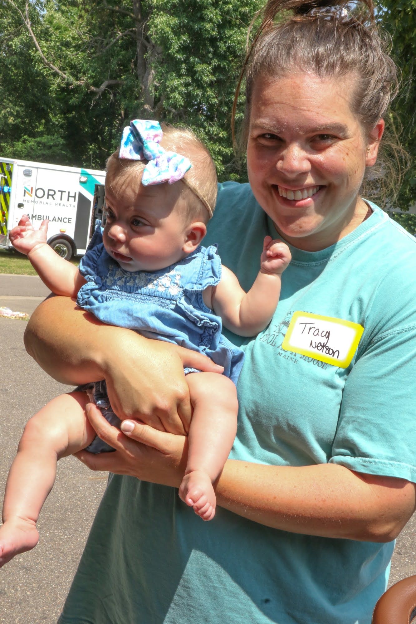Woman in teal shirt holding a baby in a blue floral outfit; both looking at the camera.