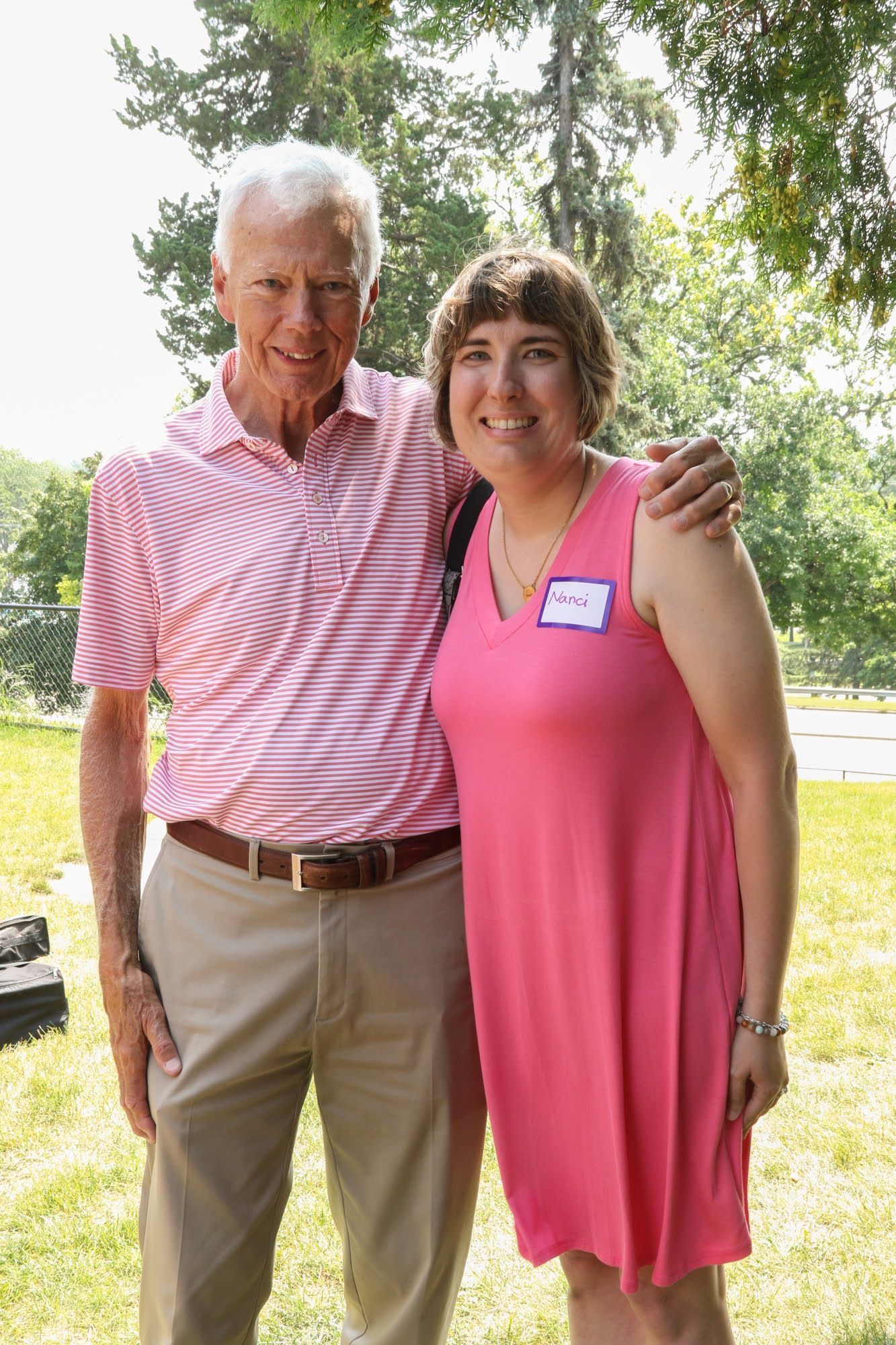 Man in pink shirt and woman in pink dress with arms around each other, outside on a sunny day.
