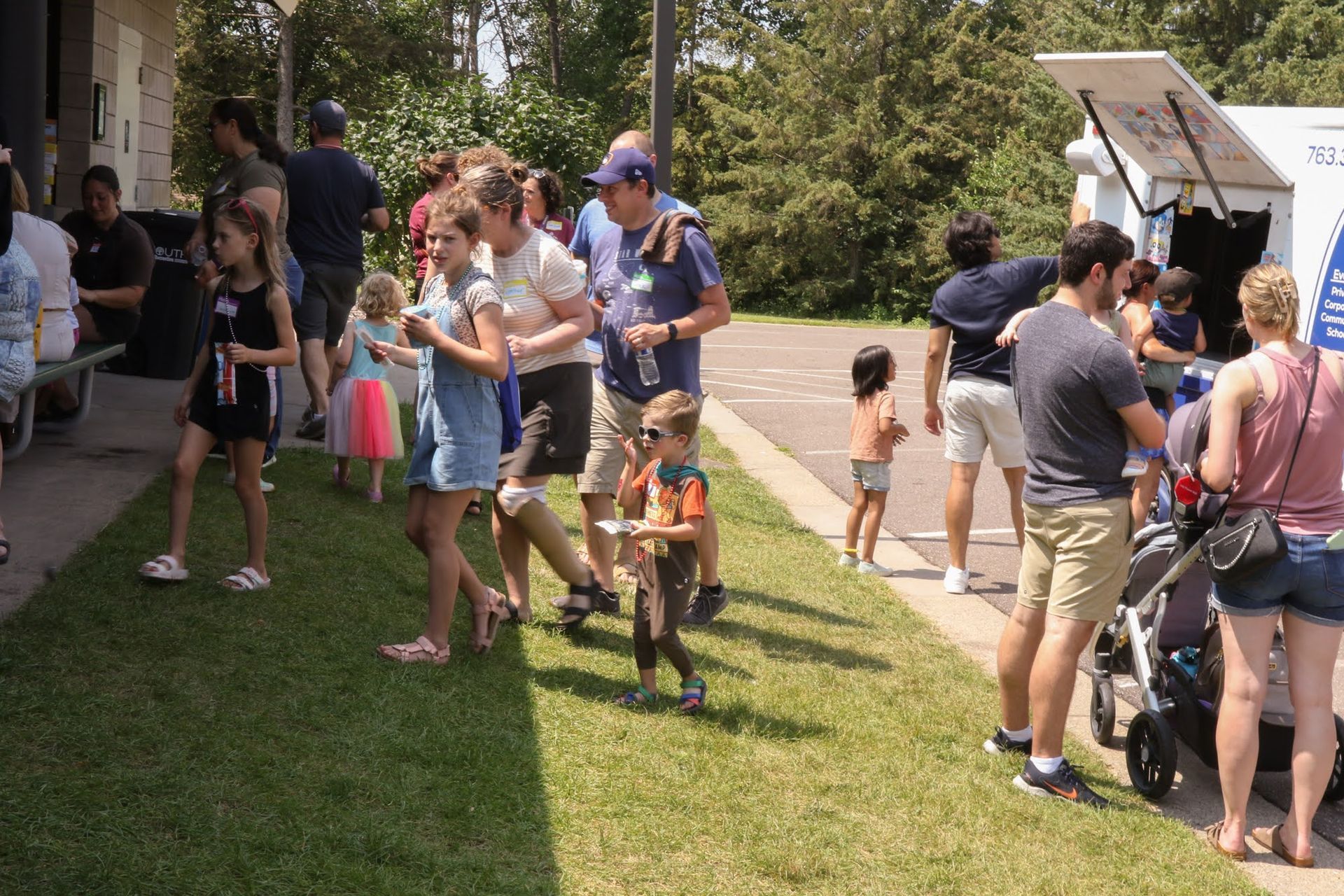 People lined up at an outdoor event with an ice cream truck. Green grass, sunny day.