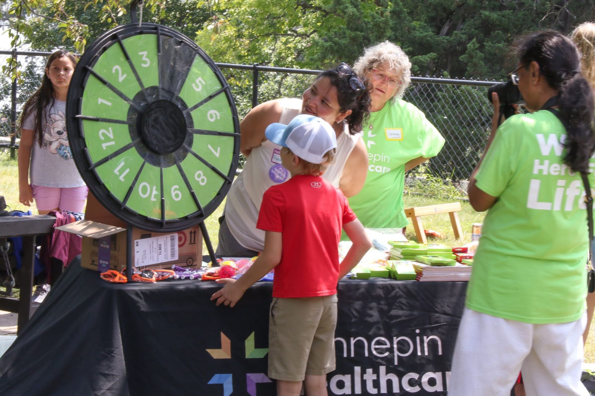 People at a Hennepin Healthcare booth with a prize wheel. A child watches the wheel being spun.