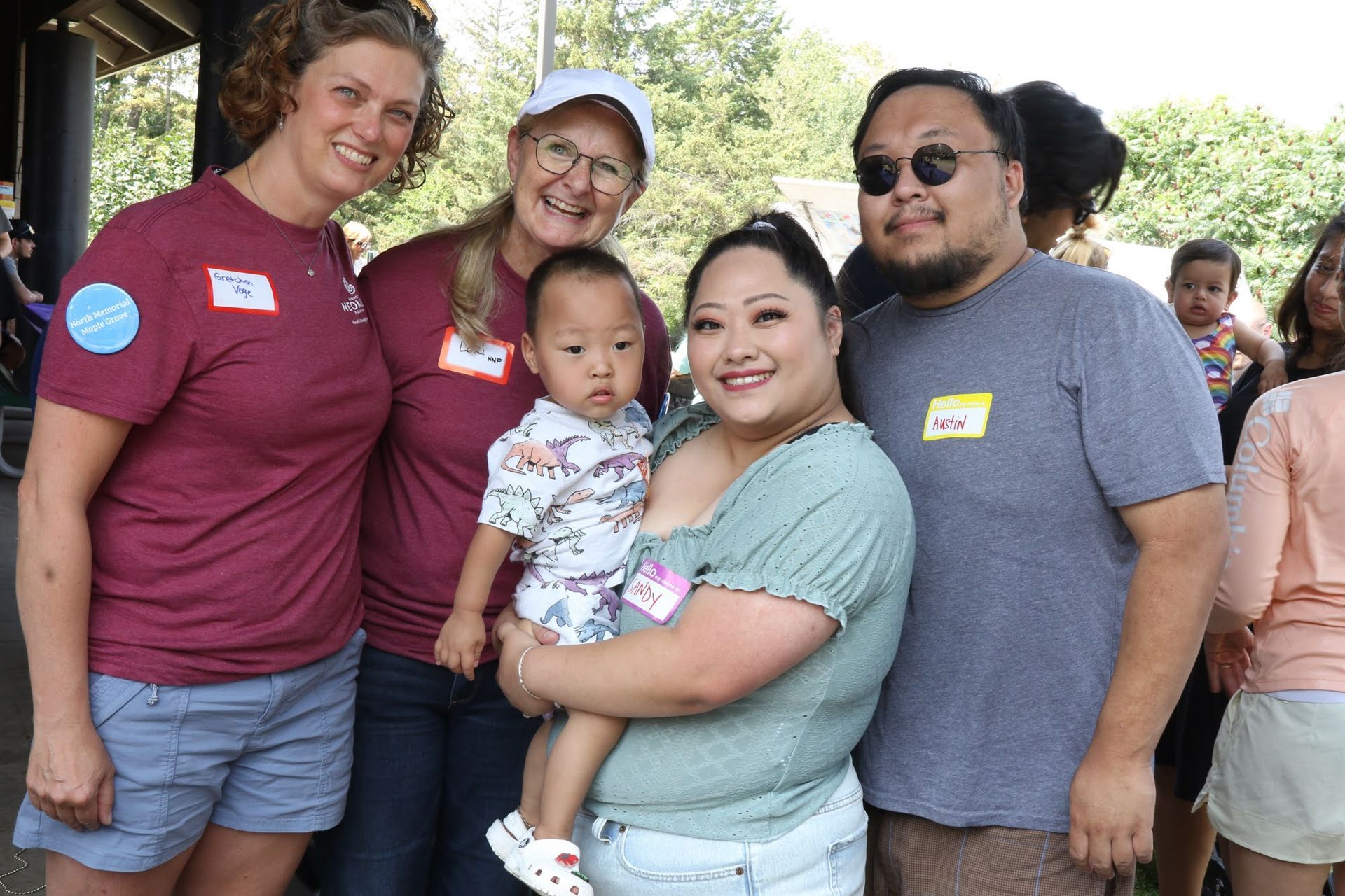 Group of people posing for a photo outdoors, one holding a baby. All are smiling.