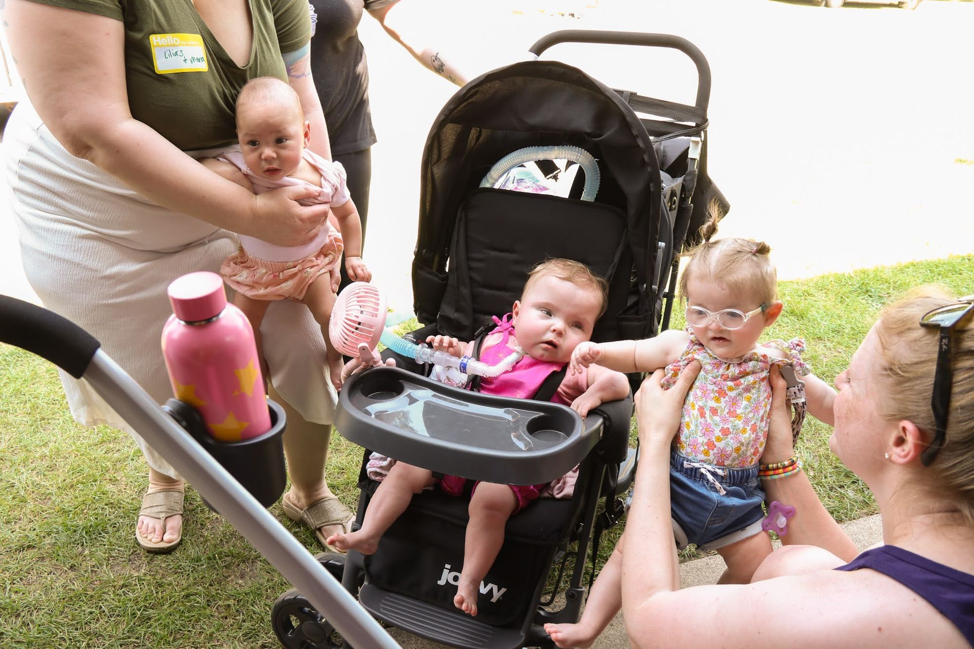 People with babies outdoors, some holding infants, others in a stroller.
