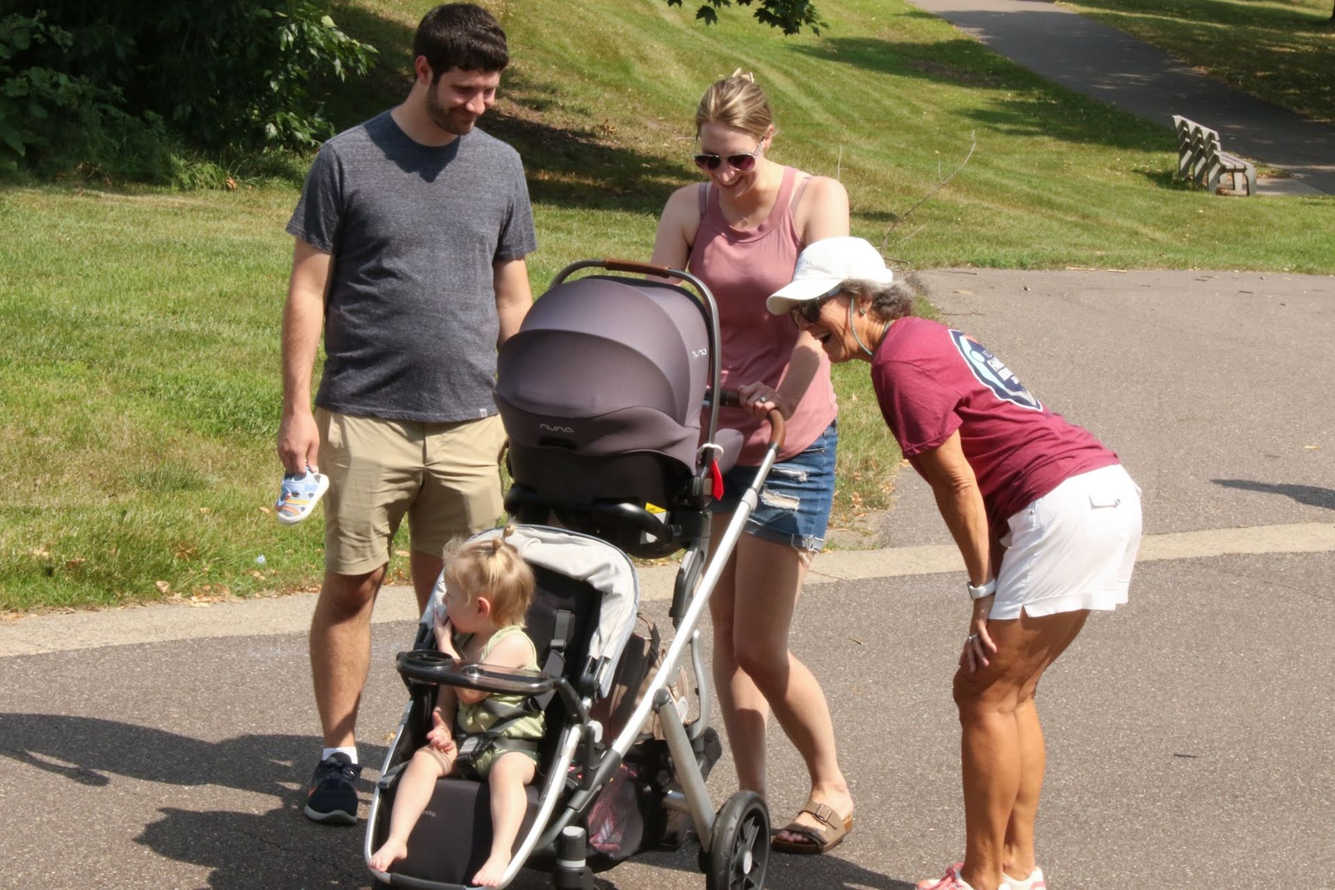 A family and an older woman looking at a baby in a stroller on a paved path.