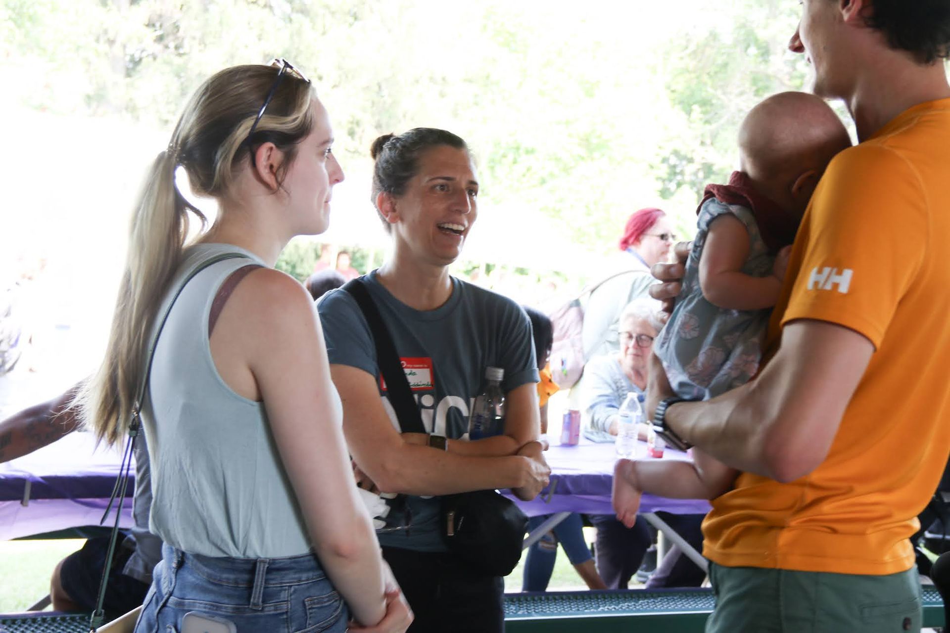 Two women and a man with a baby chatting at an outdoor event.