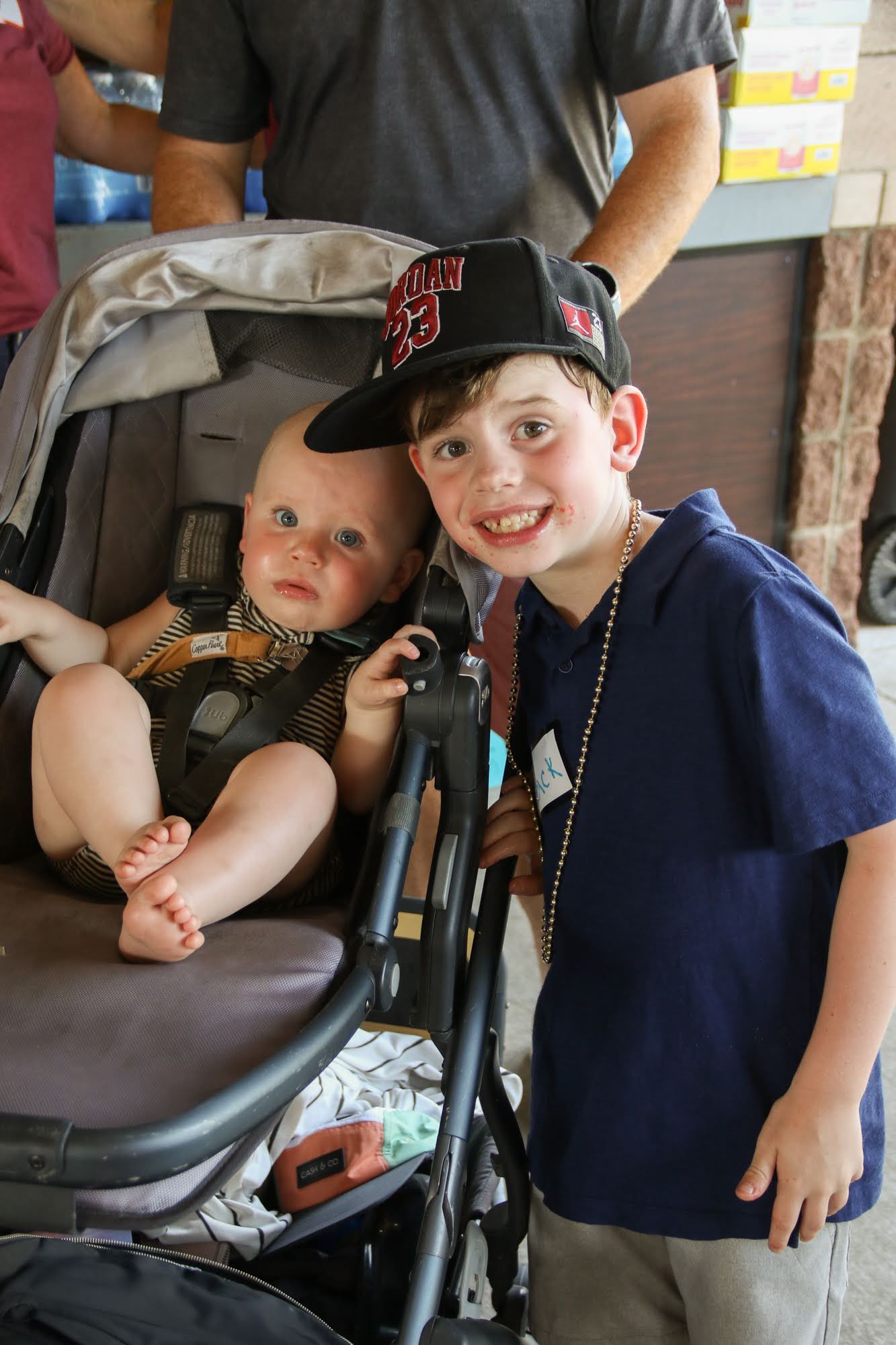 Boy in SF Giants hat smiles next to baby in stroller.