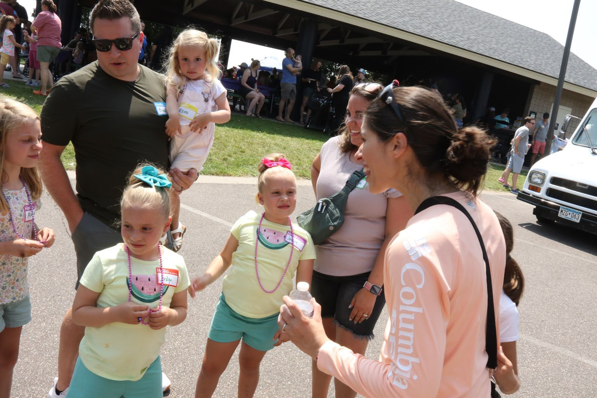People at an outdoor event, including children wearing colorful accessories, interacting with adults.