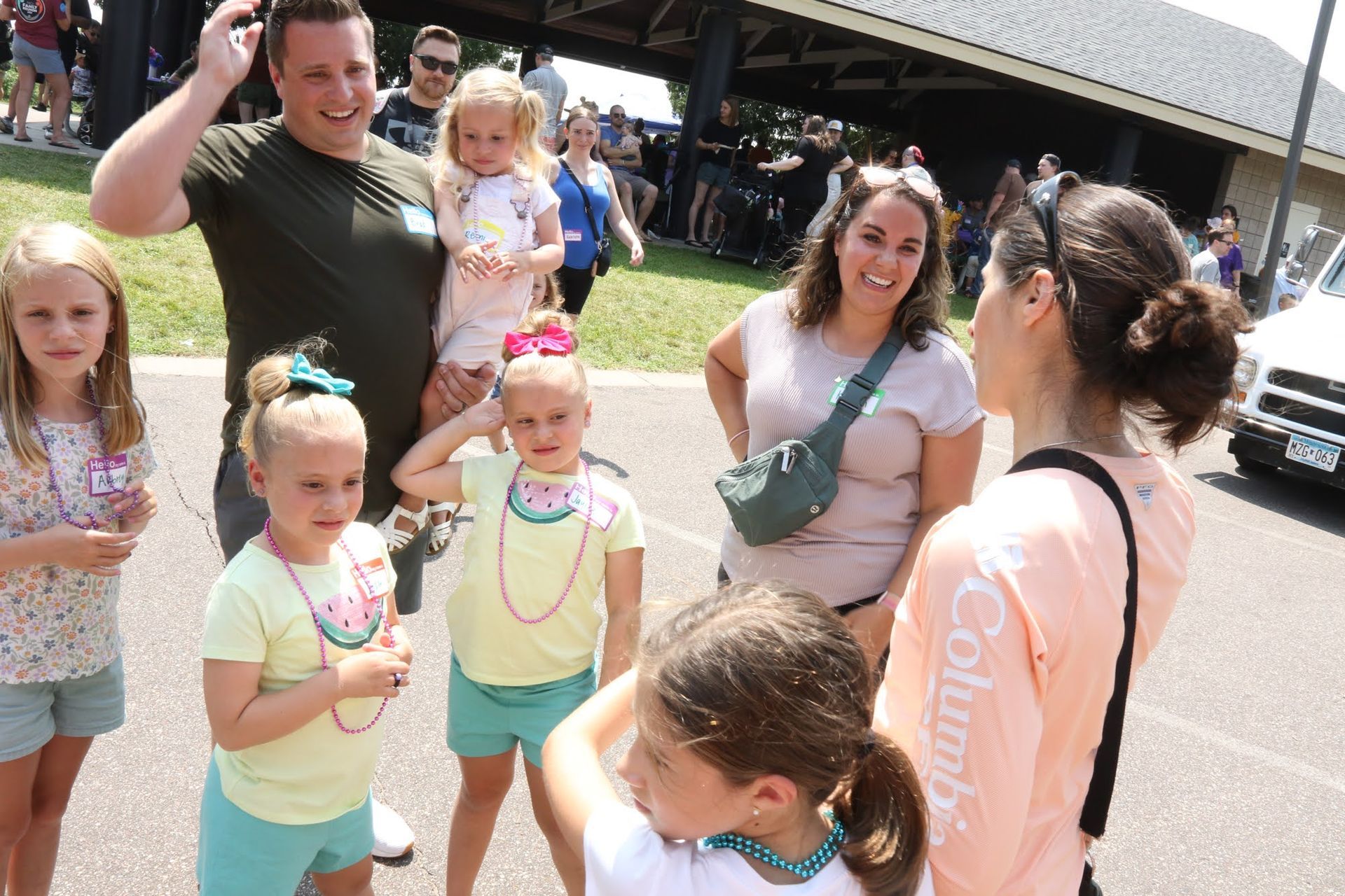 Group of people outside, smiling. Man holds a child. Other children wear bright clothes and jewelry.