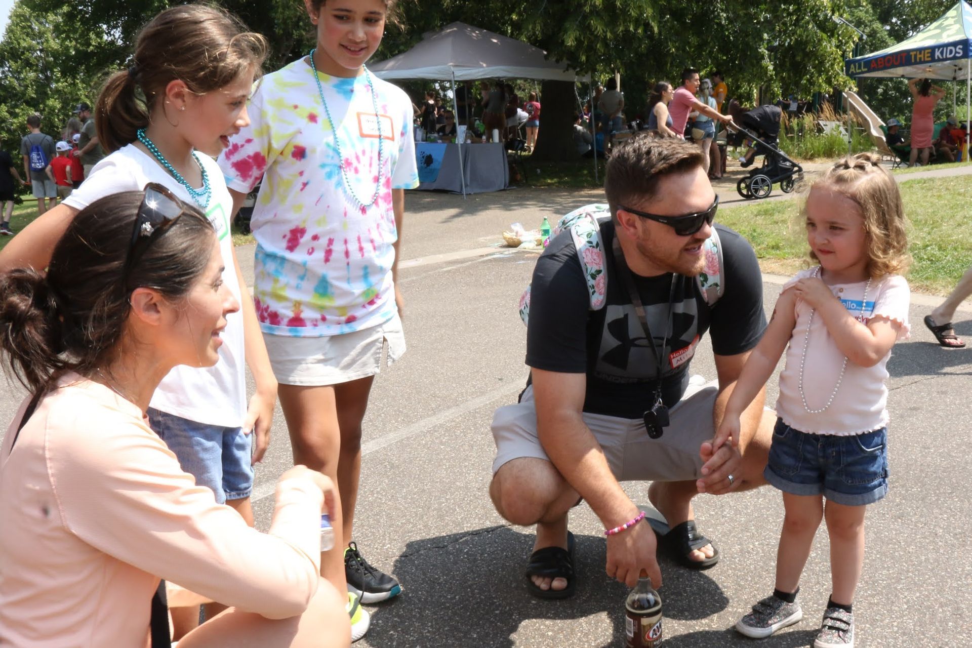 Family interacting outdoors; woman and man kneeling, talking to children. Others stand by.