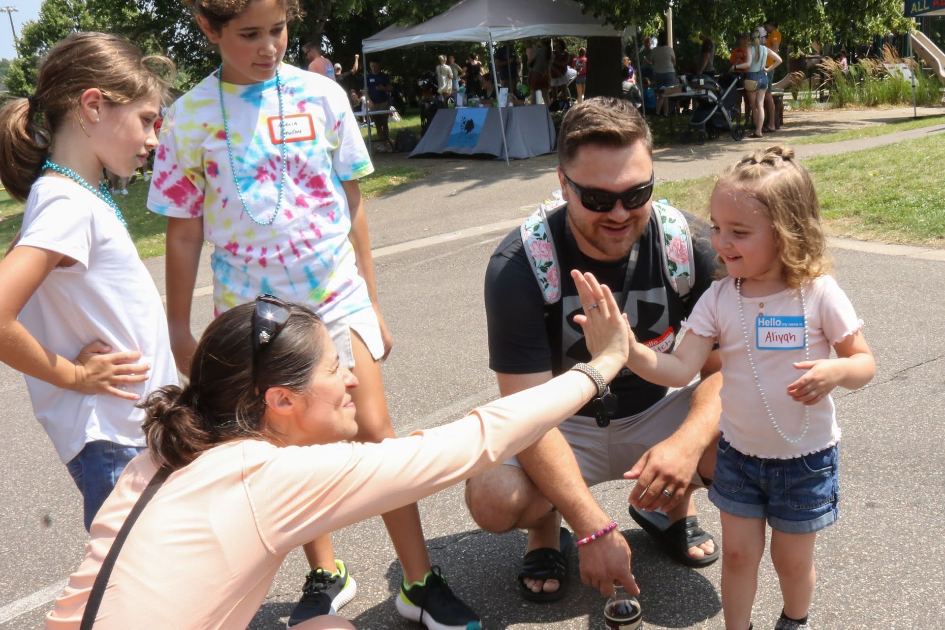 Group of people high-fiving outdoors. Smiling people, children wearing nametags. Sunny day.