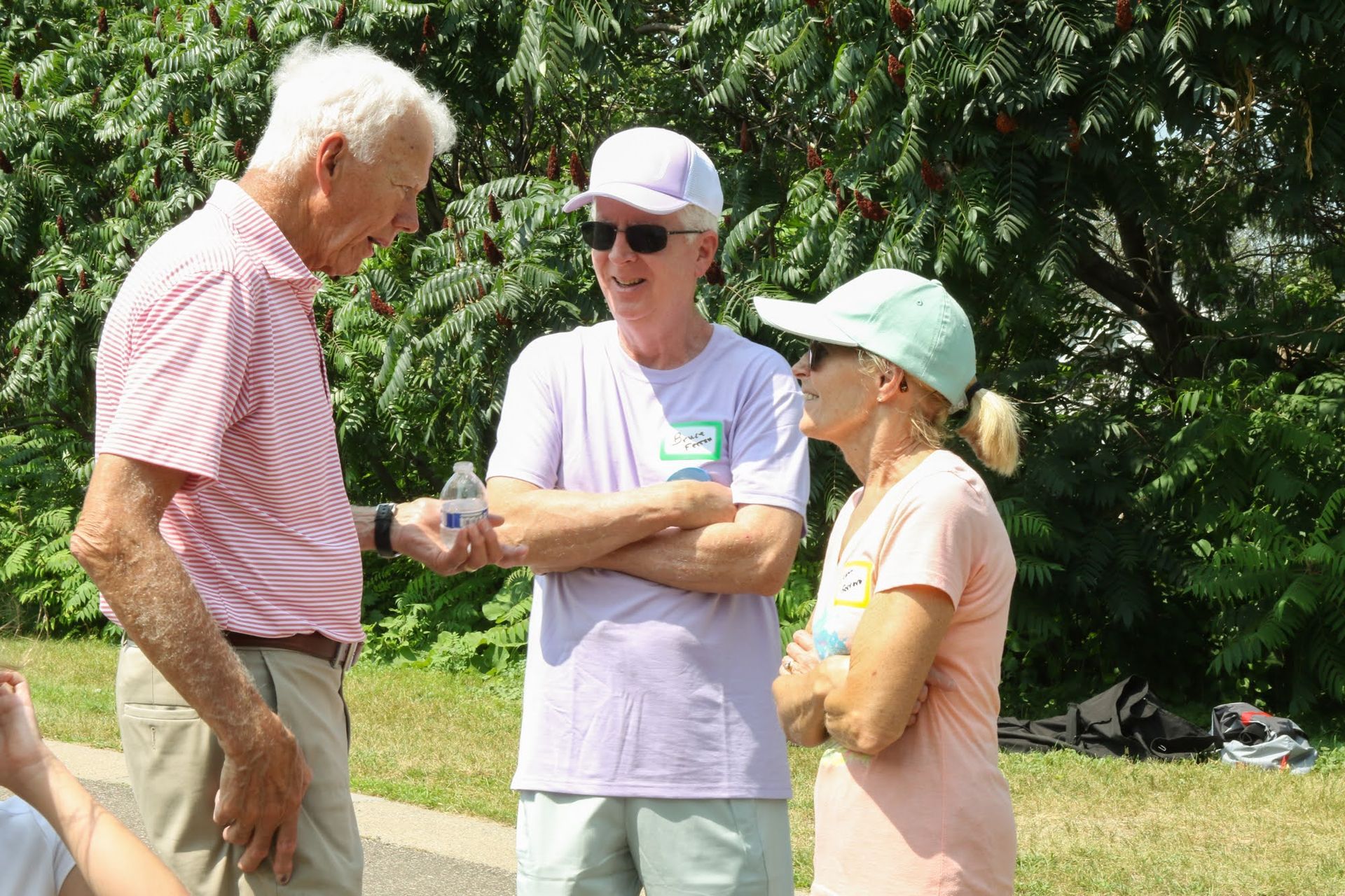 Three people in casual wear talking outdoors near greenery.