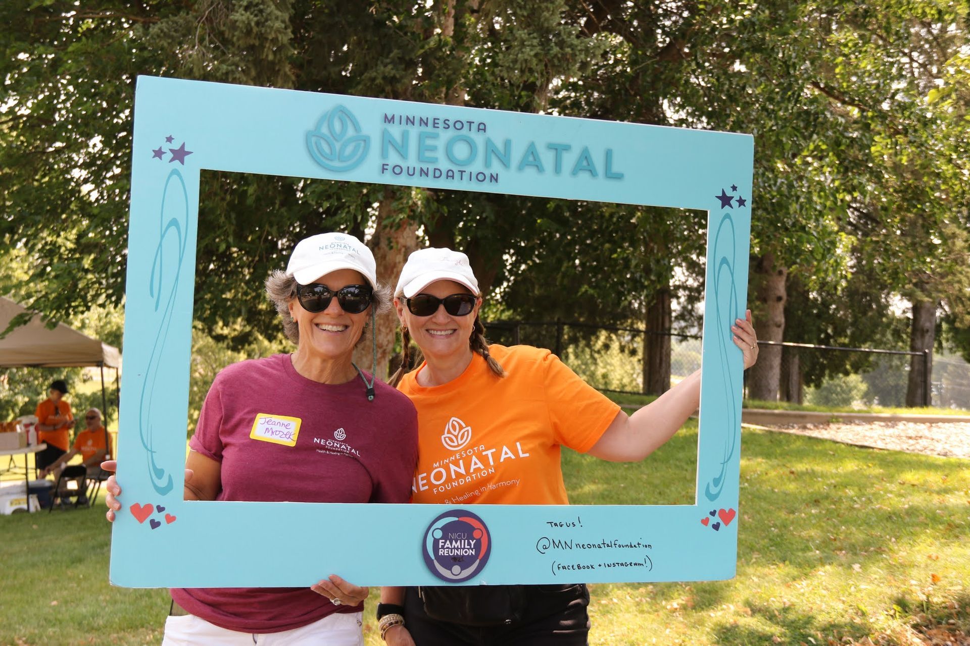 Two women hold a blue photo frame outdoors for the Minnesota Neonatal Foundation event.