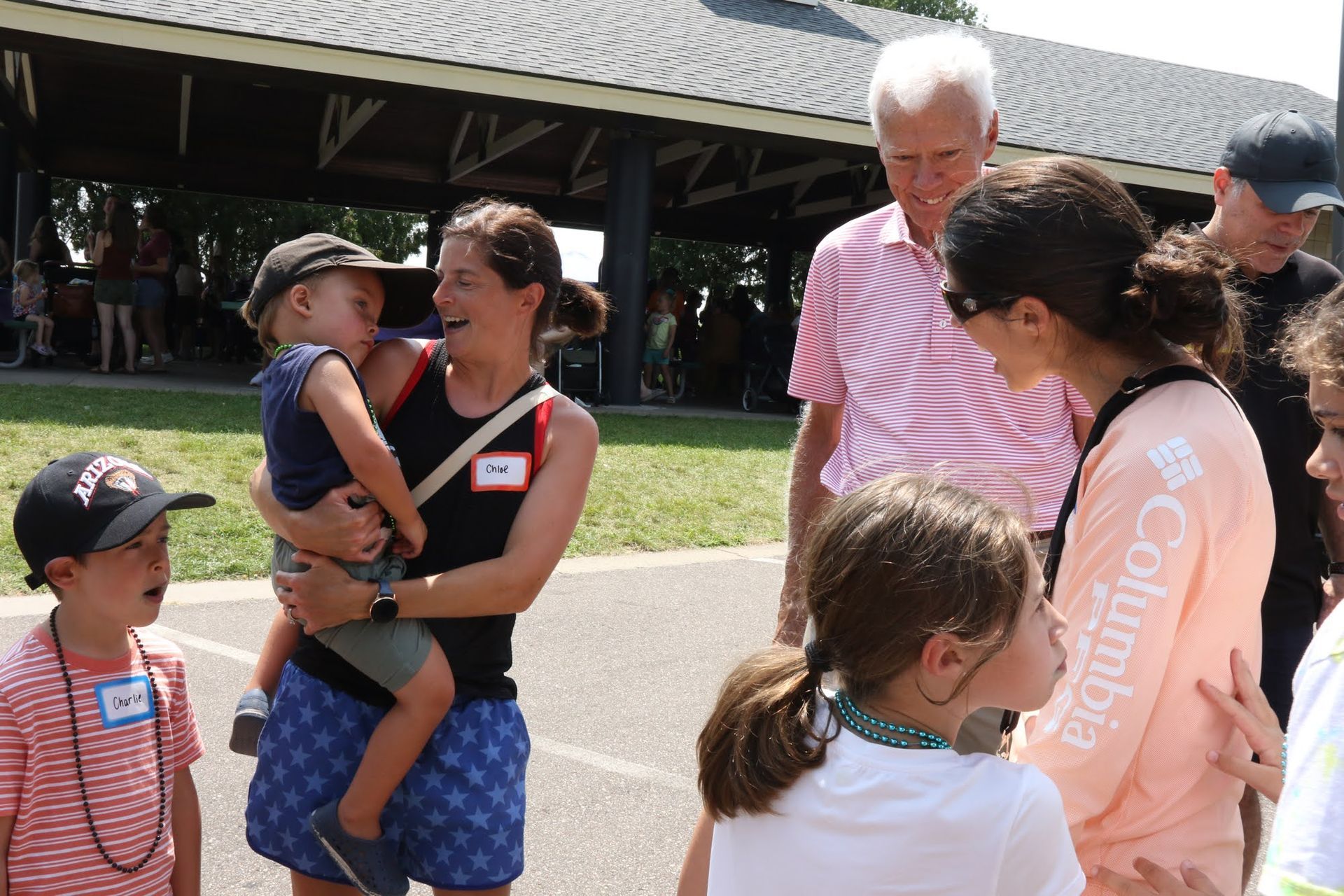 People at a park: Woman holding child, talking to another woman and a man.