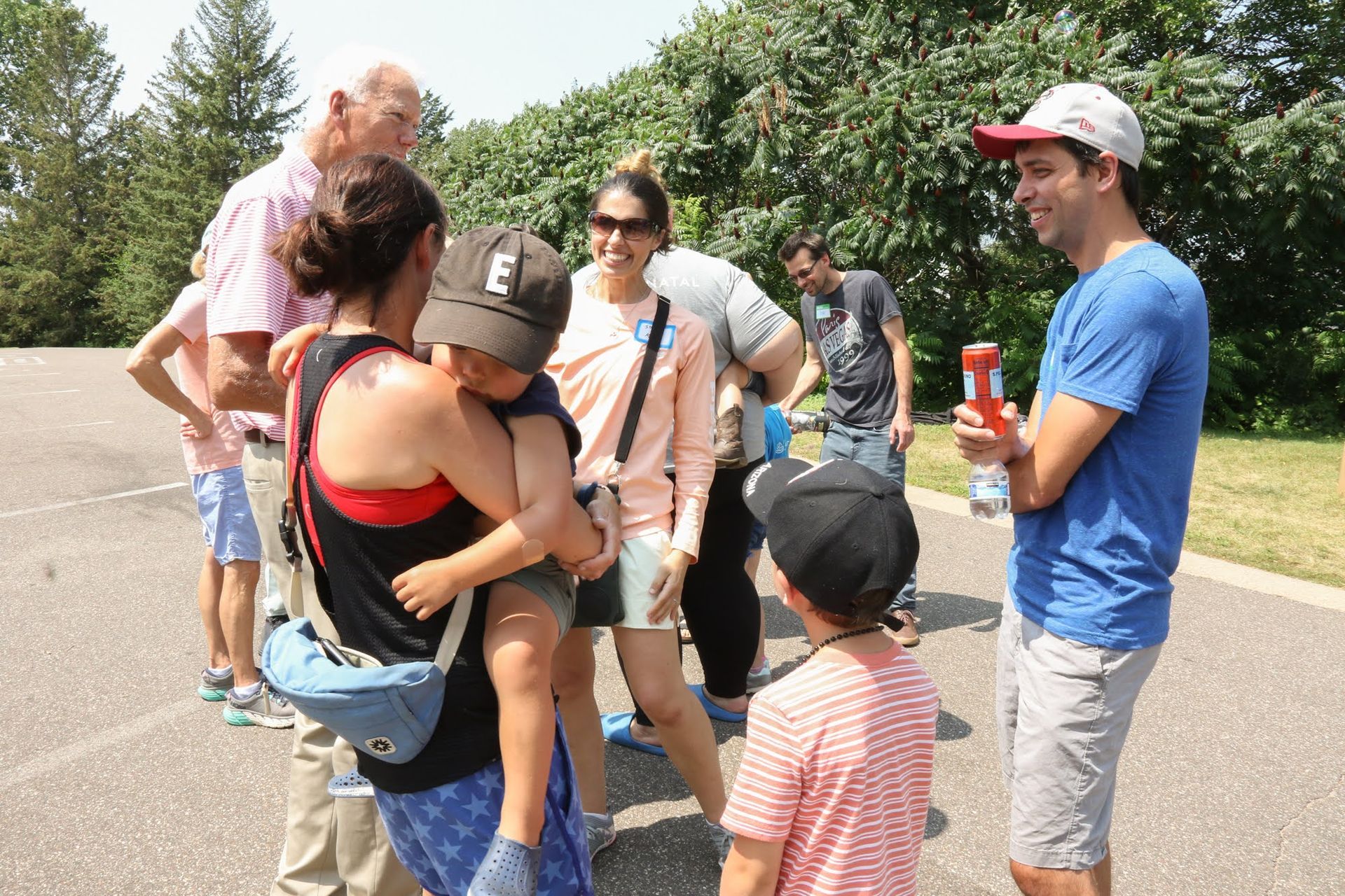 Group of people gathered outdoors; some smiling, a child is being held, another child in front.
