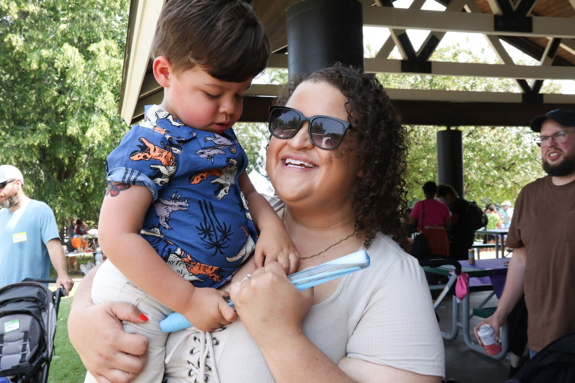 Woman smiling, holding child at outdoor event.