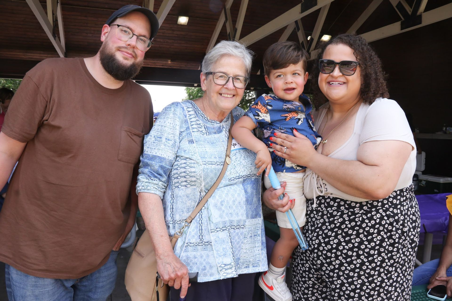 Family poses outdoors, smiling. A man, woman, child, and another woman stand together.