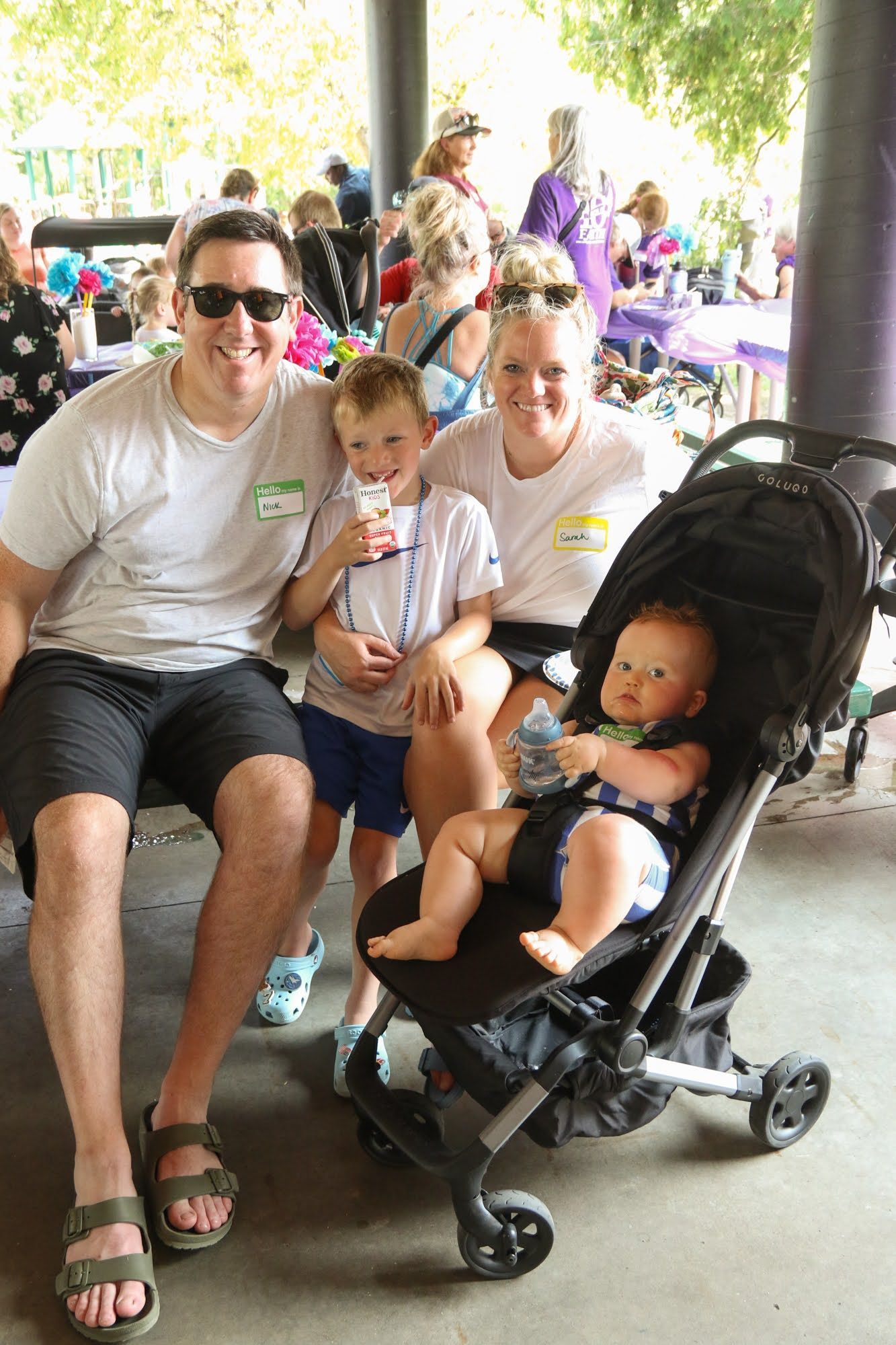 Family with two children at outdoor event. Boy drinks from a cup, baby in stroller.