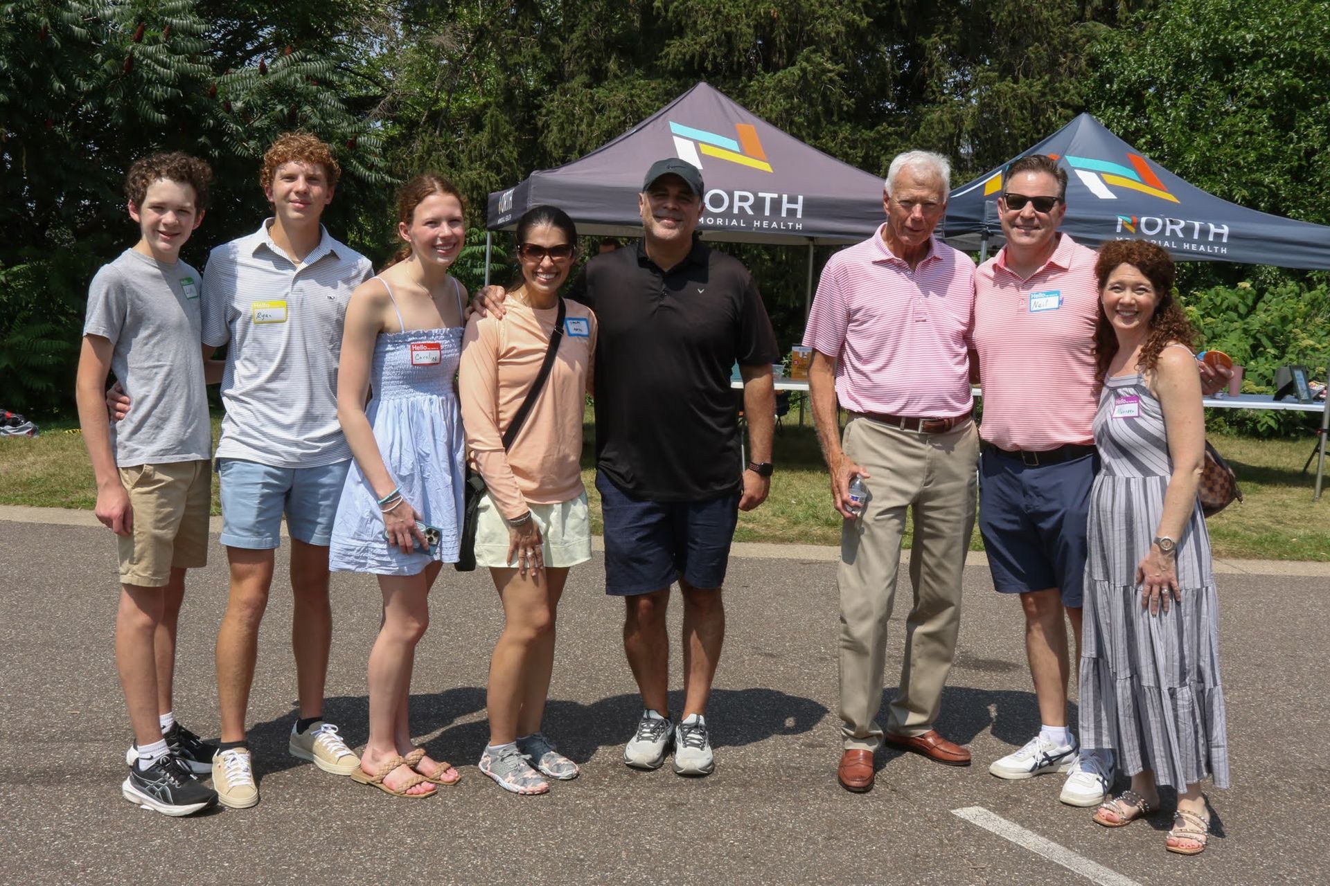 Group of people posing outdoors in front of event tents. Sunny day.
