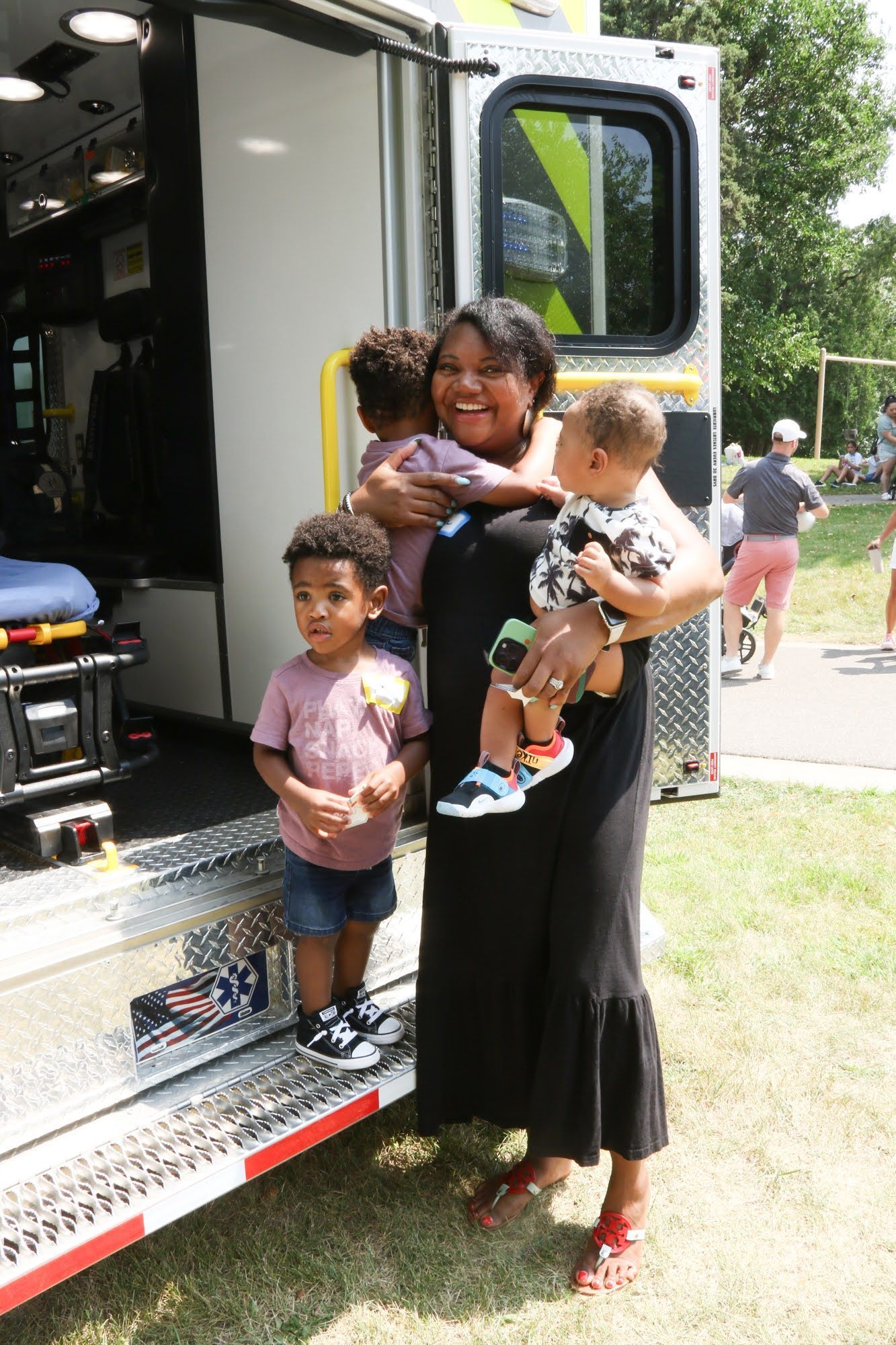 Woman with three children poses near an open ambulance. The children wear casual clothes.