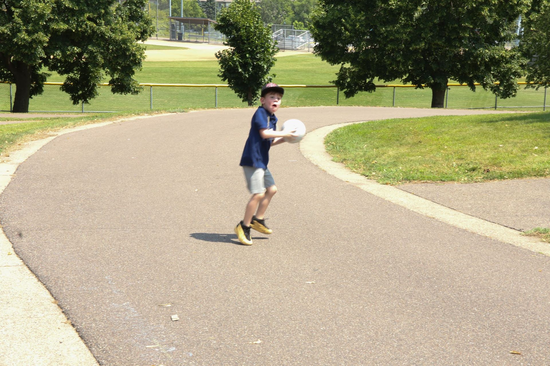 Boy throwing a frisbee on a paved path in a park on a sunny day.