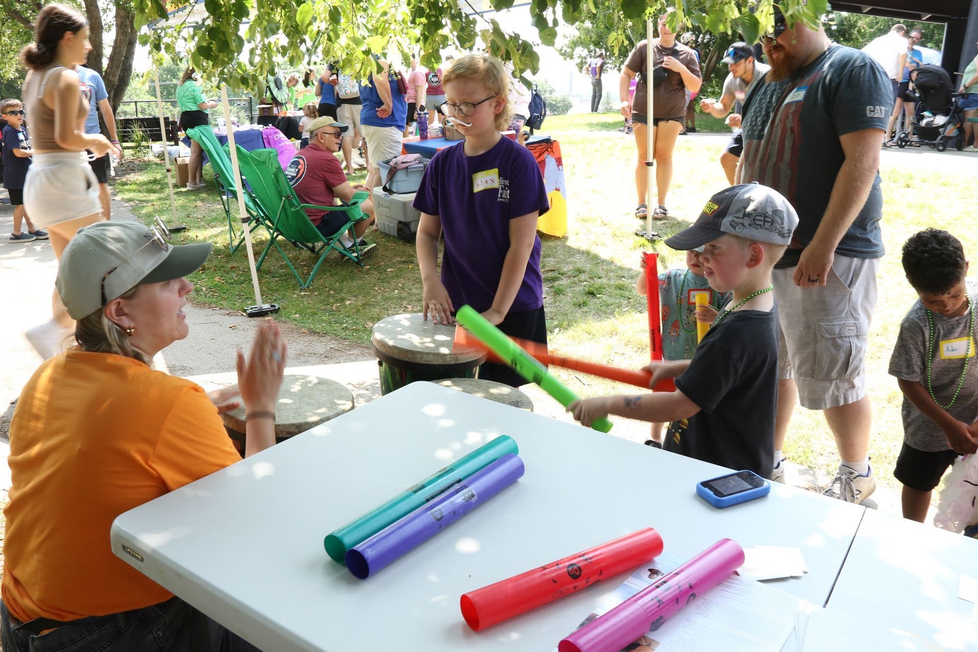 Children play drums and percussion instruments at an outdoor event with an instructor.