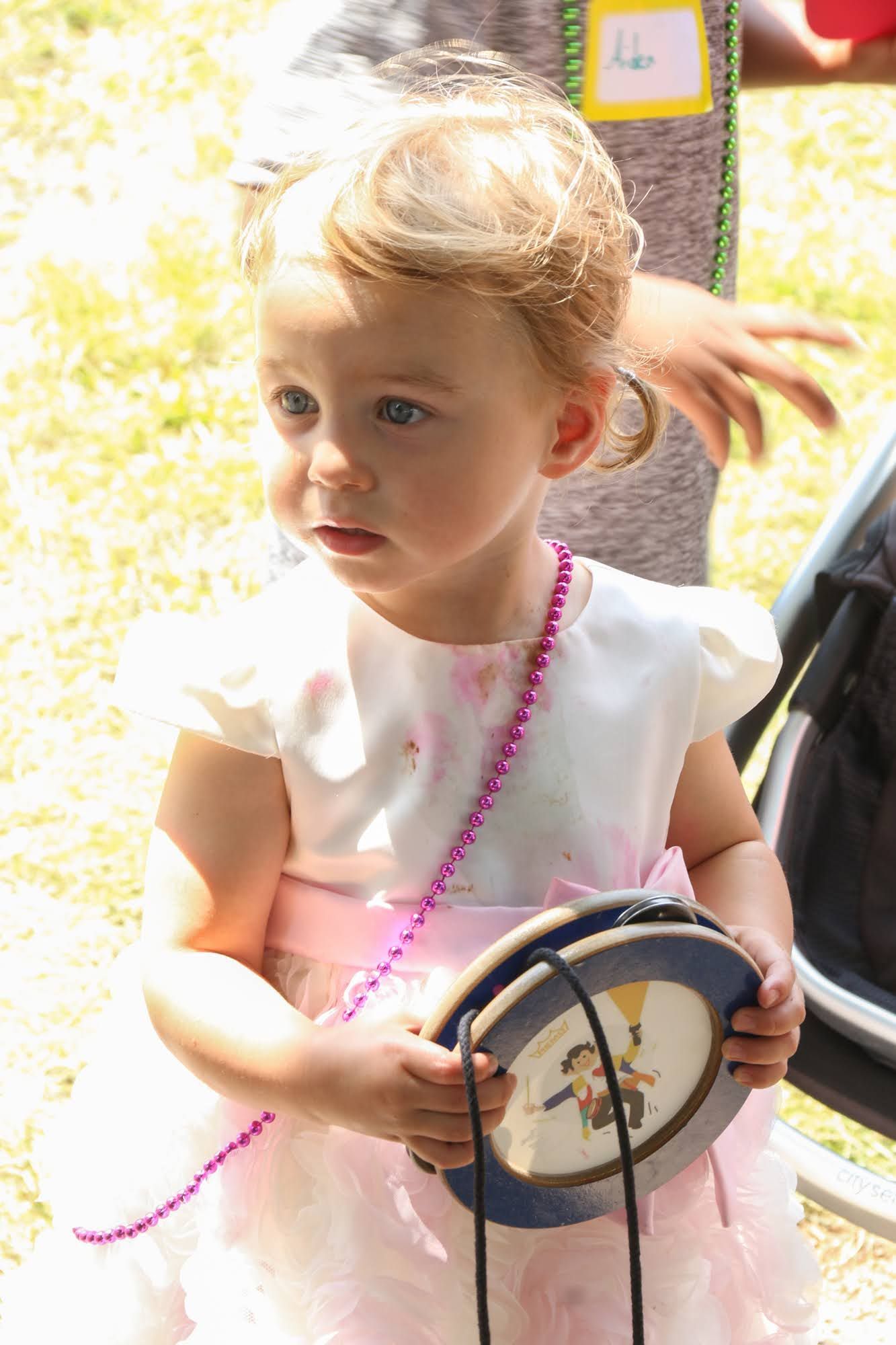 Young child in a white and pink dress, holding a small round purse with a beaded strap, looking to the side.