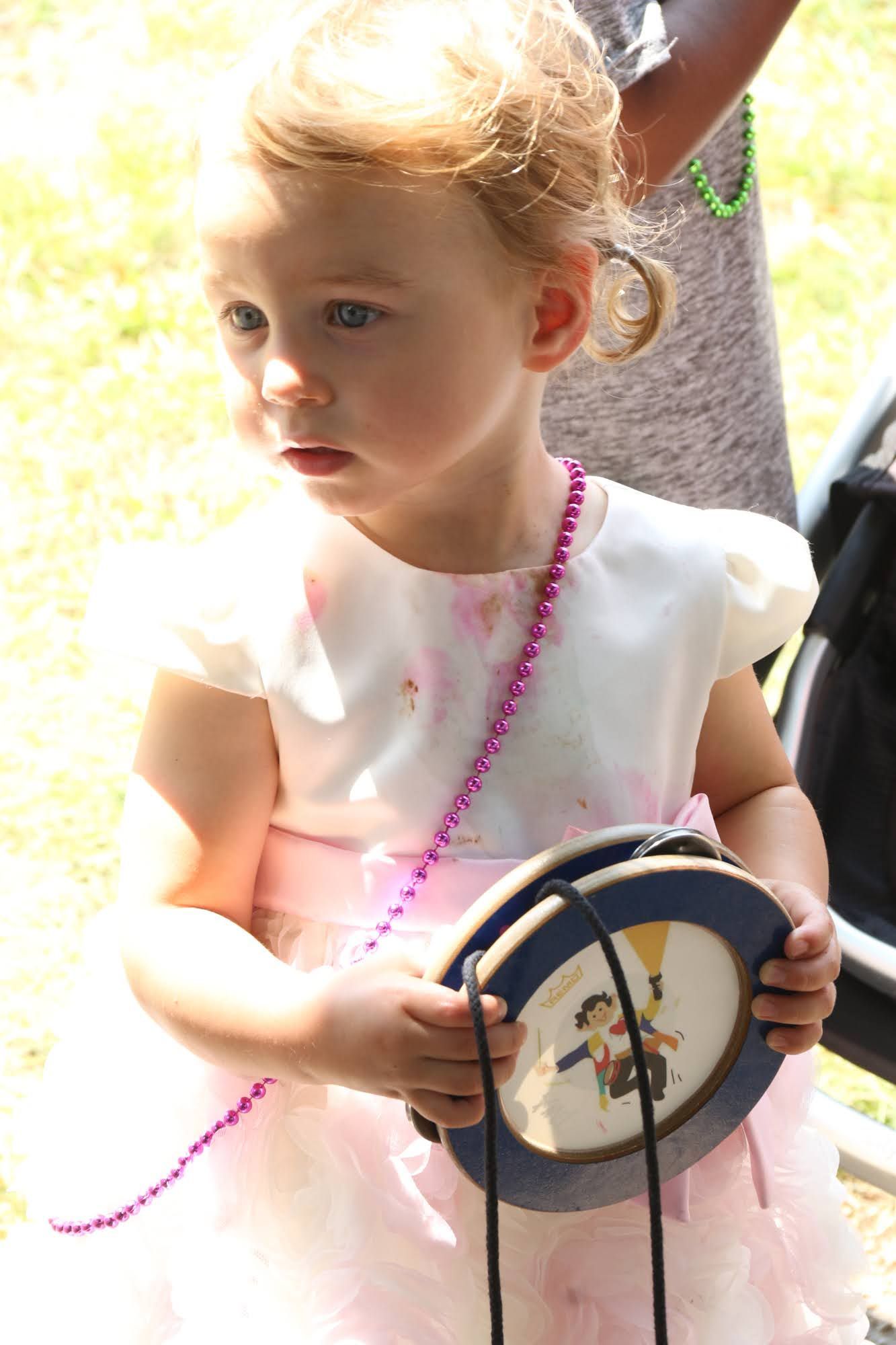 Young child in white and pink dress holding a round, painted object with a string.