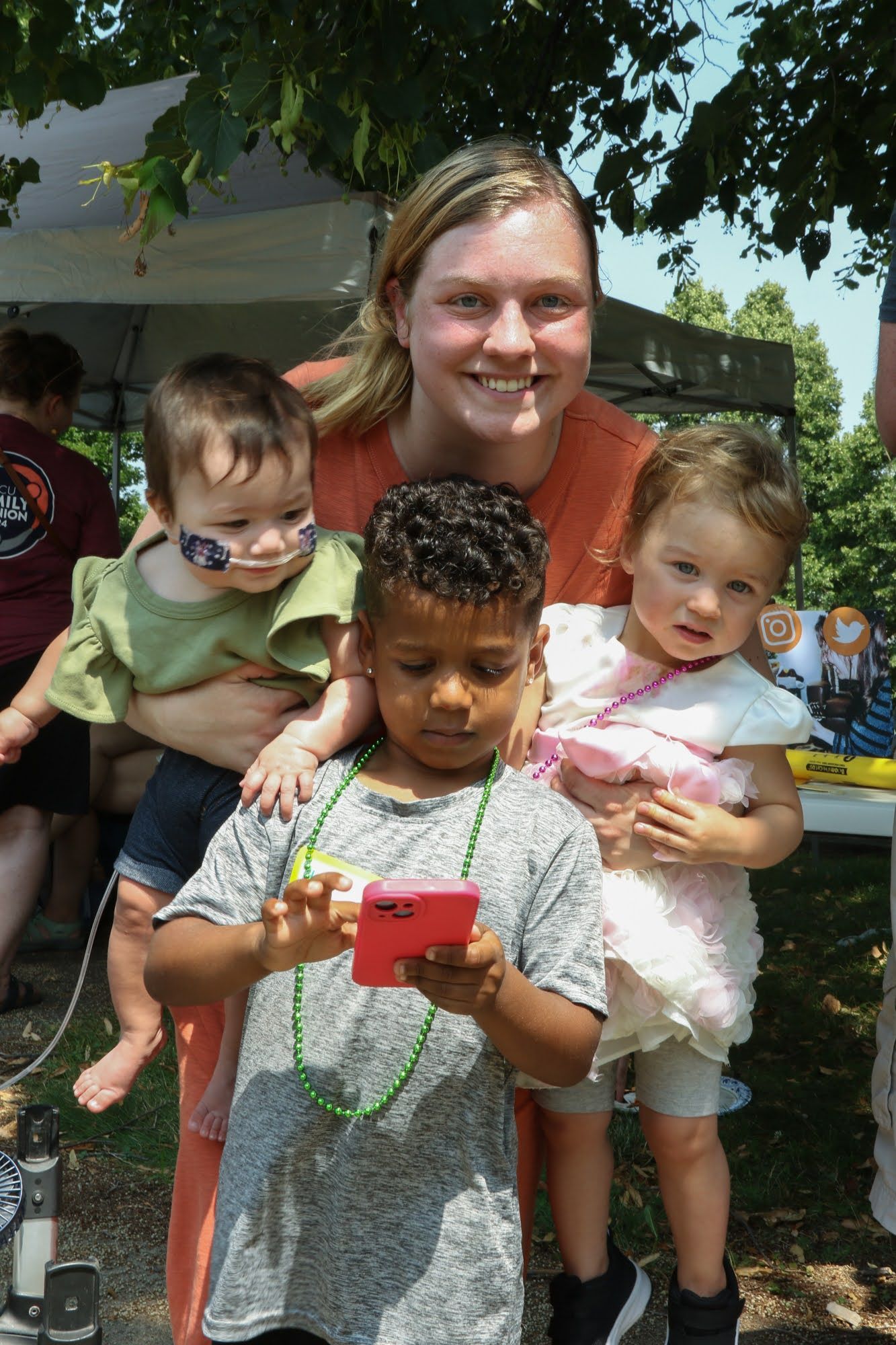 Woman holding two children smiles at camera while a boy plays with a phone.