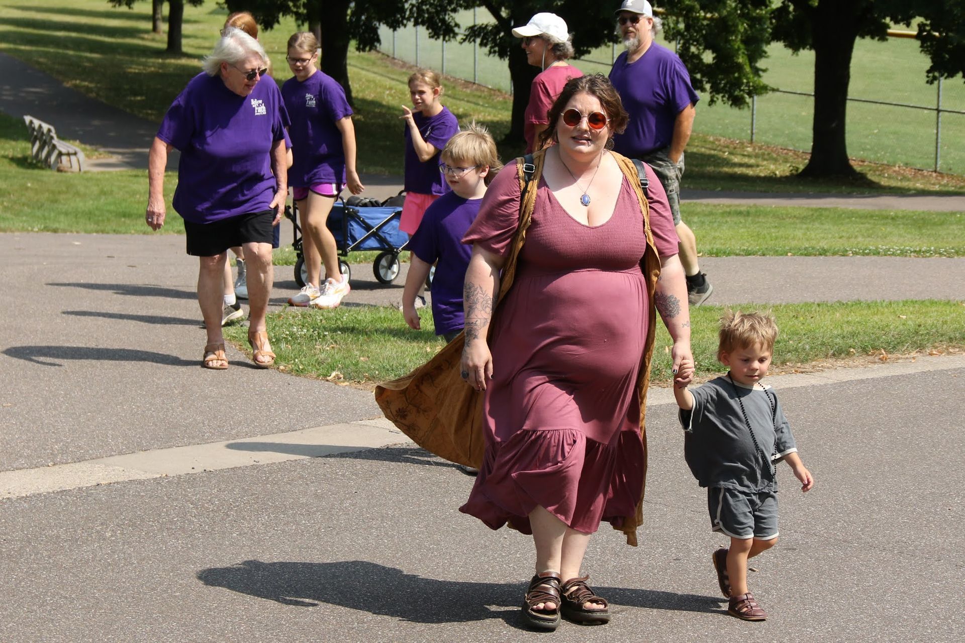A group walking outdoors; woman in burgundy dress and boy hold hands, others in purple shirts.