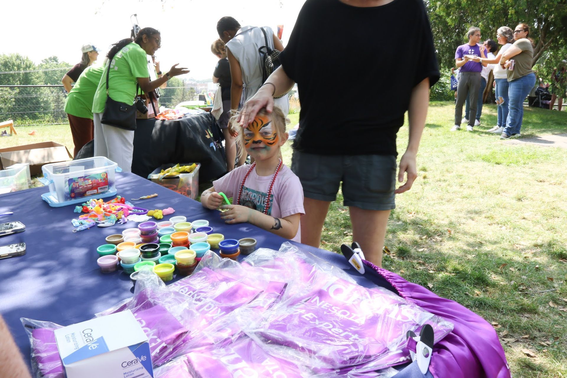 Child with tiger face paint at craft table; people in background.