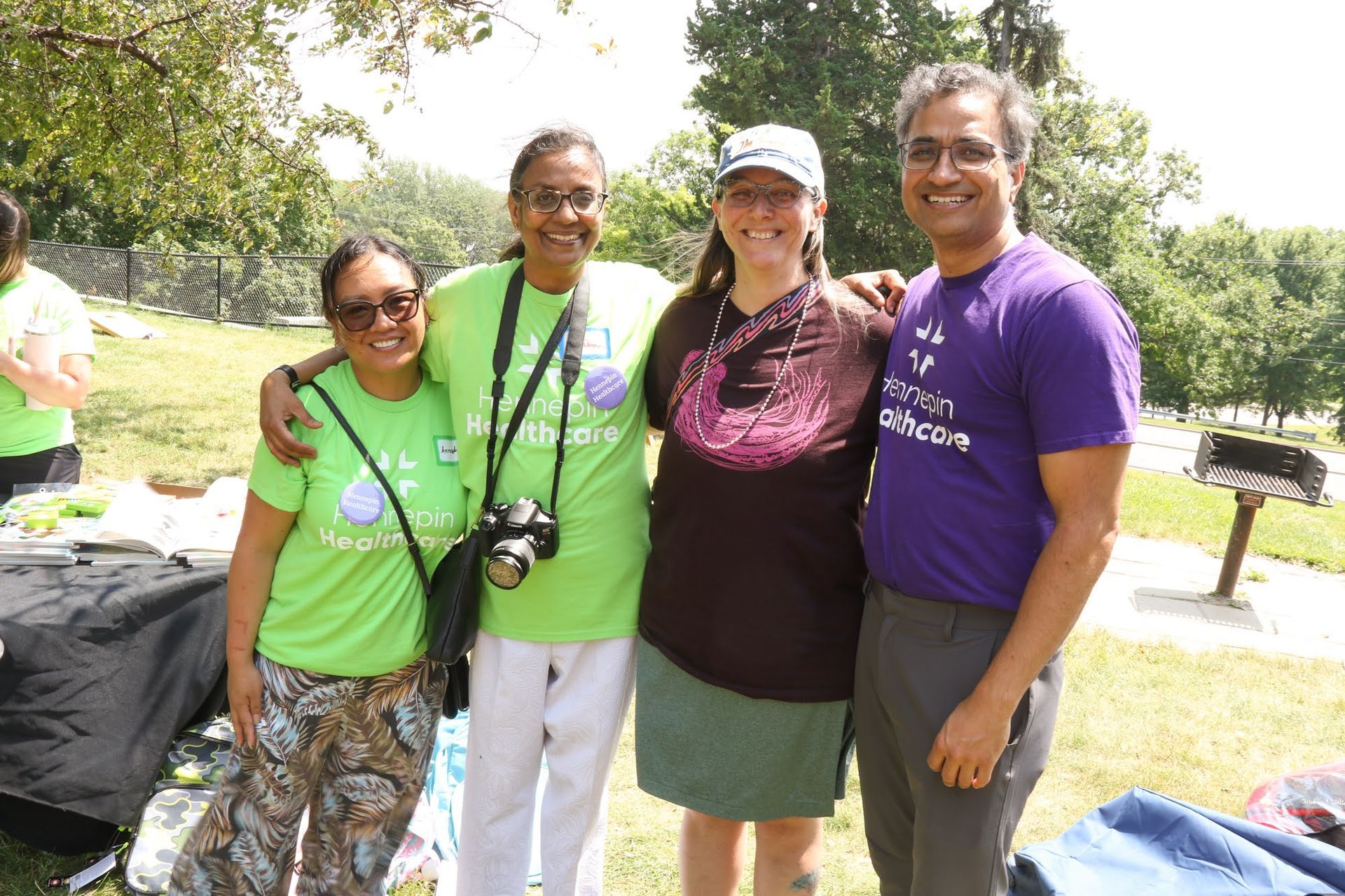 Four people smiling, posing outdoors. Green shirts, park setting.