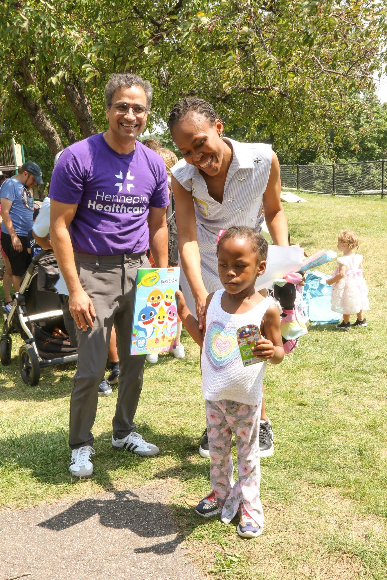 Man in purple shirt, woman, and child in park, smiling. Giving the child gifts.