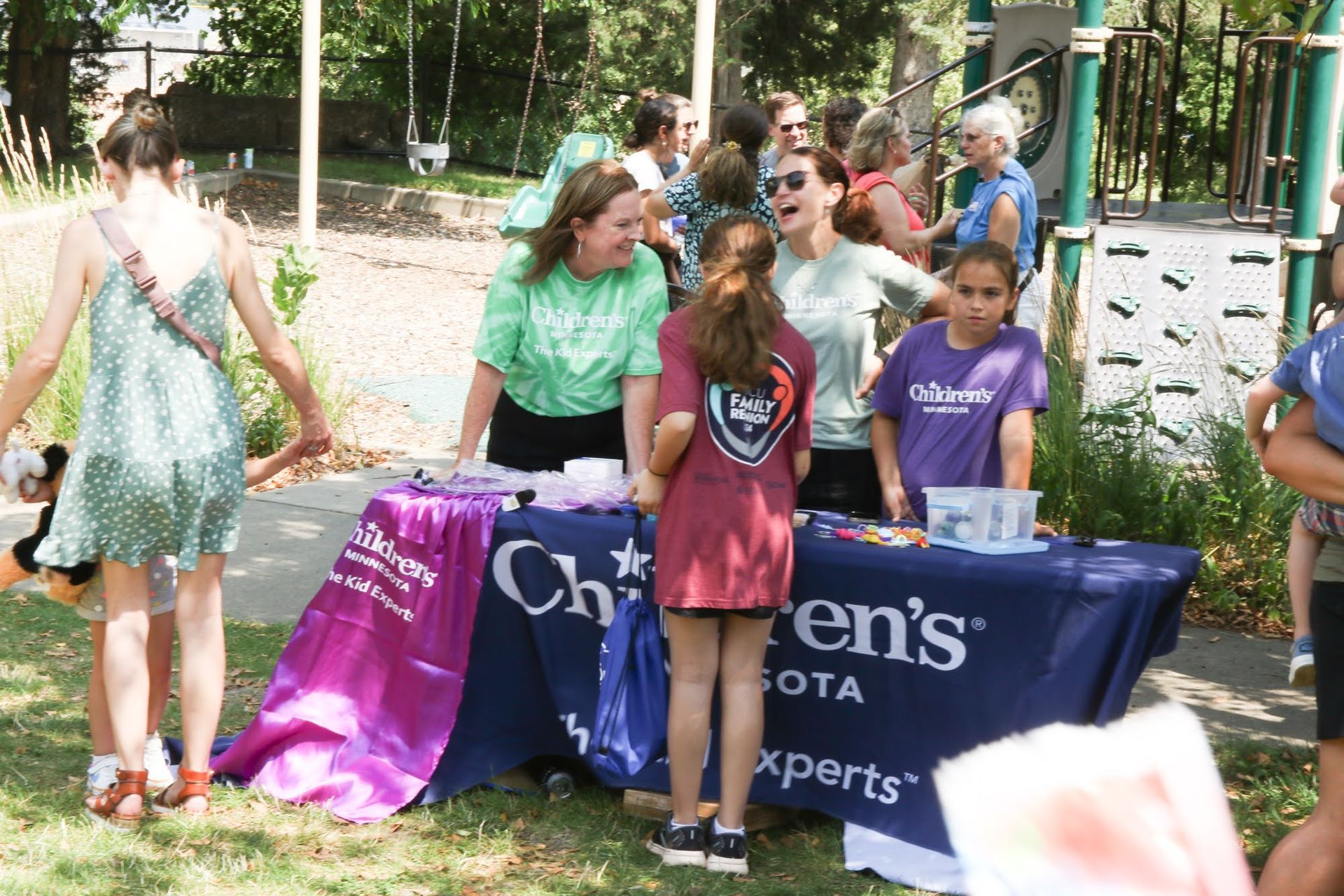 People at an outdoor Children's Minnesota booth. Several people are at the table, others are nearby, some are talking.