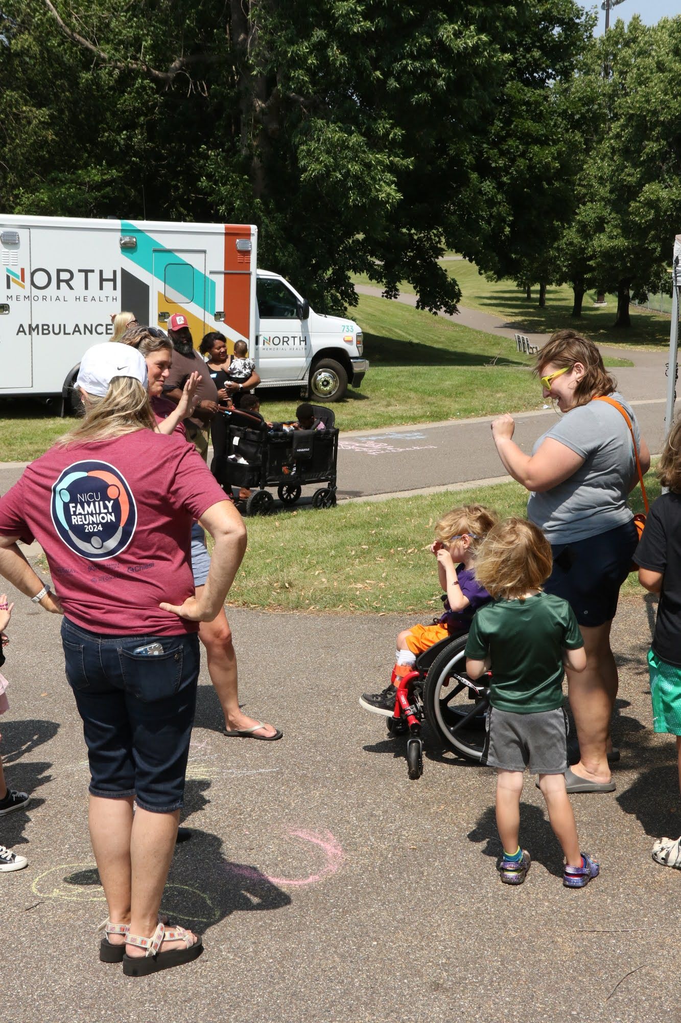 People gathered outside, near an ambulance. A child in a wheelchair is present, along with adults and other children.