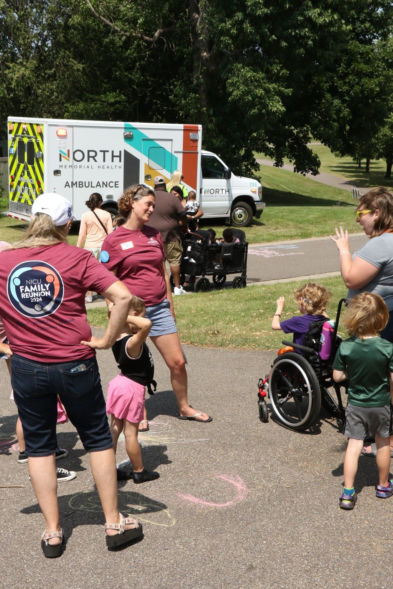 People and children near an ambulance in a park. One child is in a wheelchair.