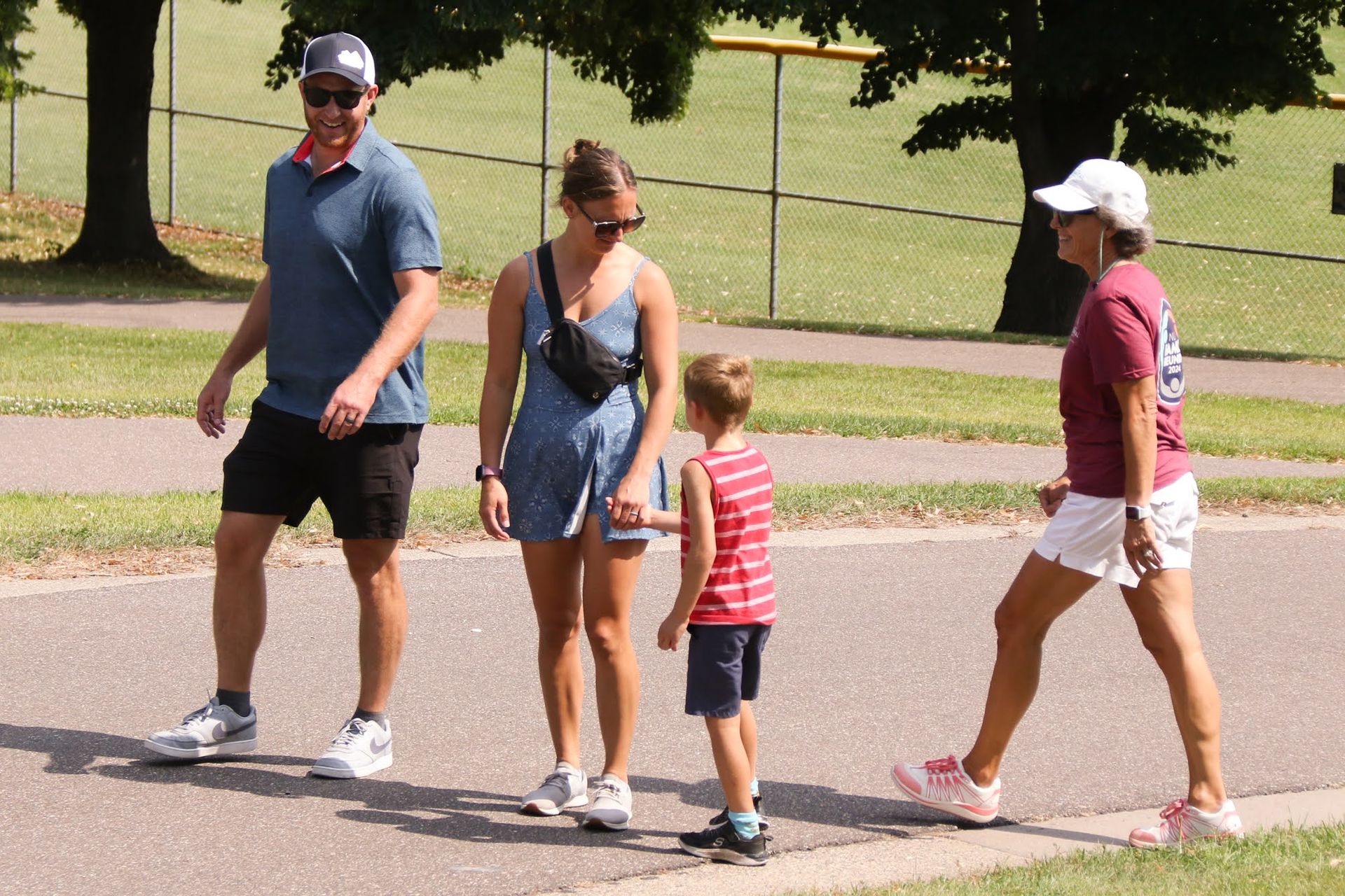 Four people walking on a path in a park; a man, woman, child, and another woman.