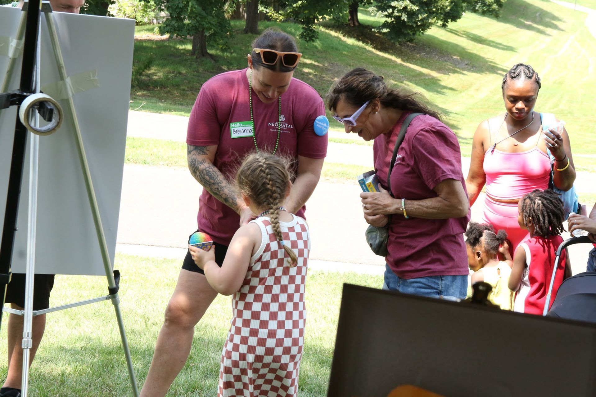 A person assists a child with an art project outdoors; others watch.