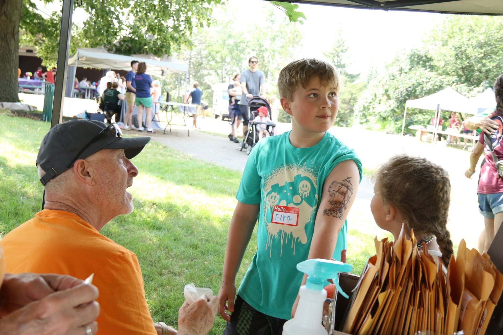 Boy with temporary tattoo, talking to an older man outdoors. Another child stands nearby.